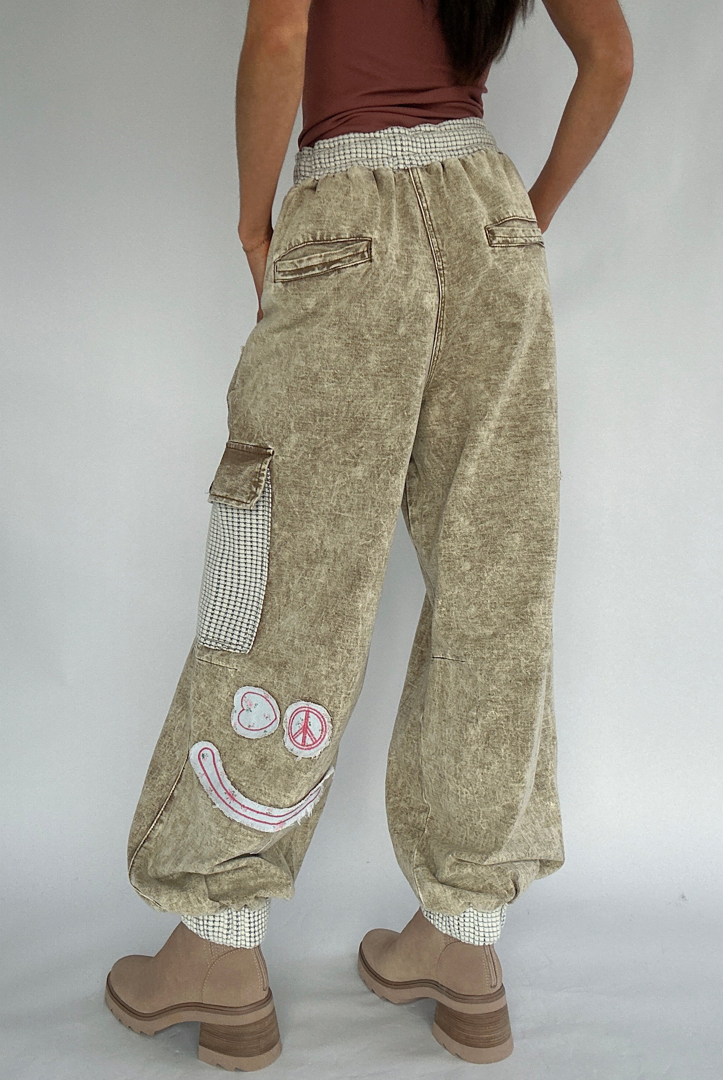 Person wearing beige cargo pants with smiley patches on a plain background from back