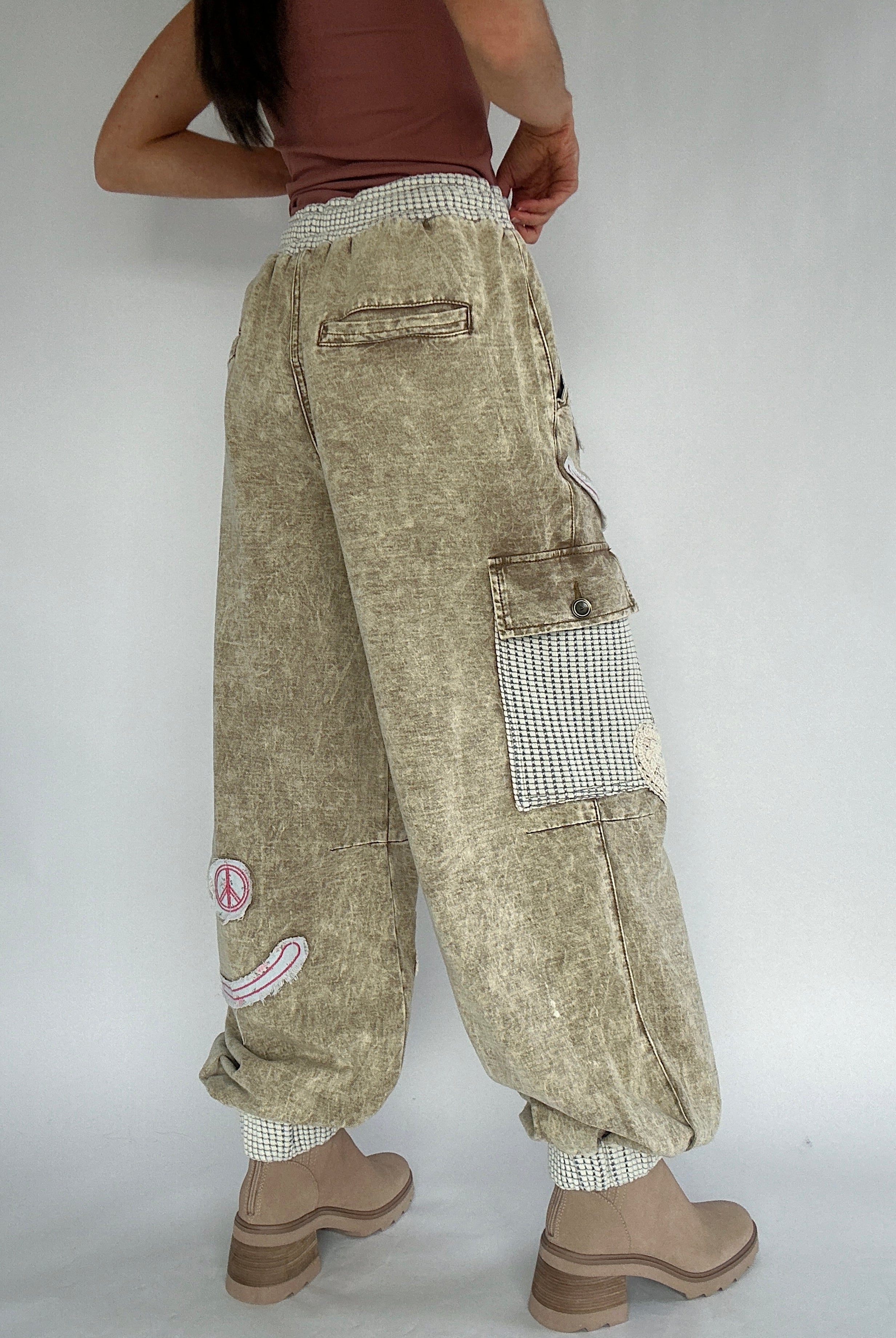 Person wearing beige cargo pants with patches on a plain background