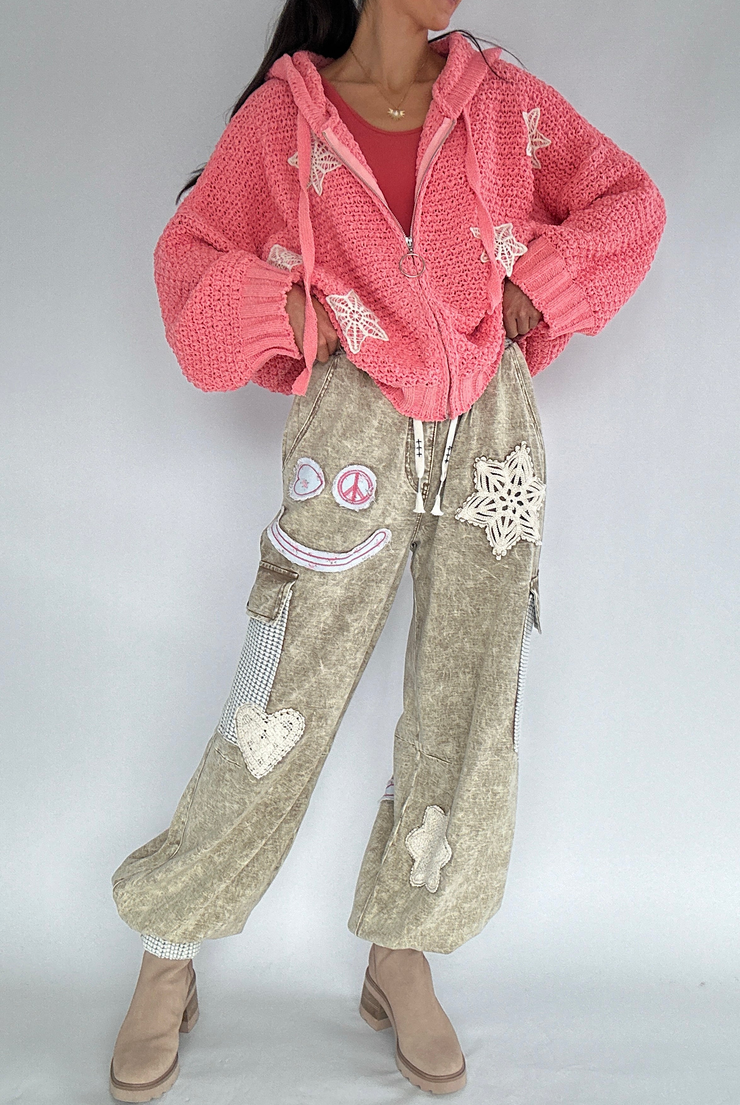 Person wearing a pink cardigan and beige cargo pants with decorative patches on a plain background
