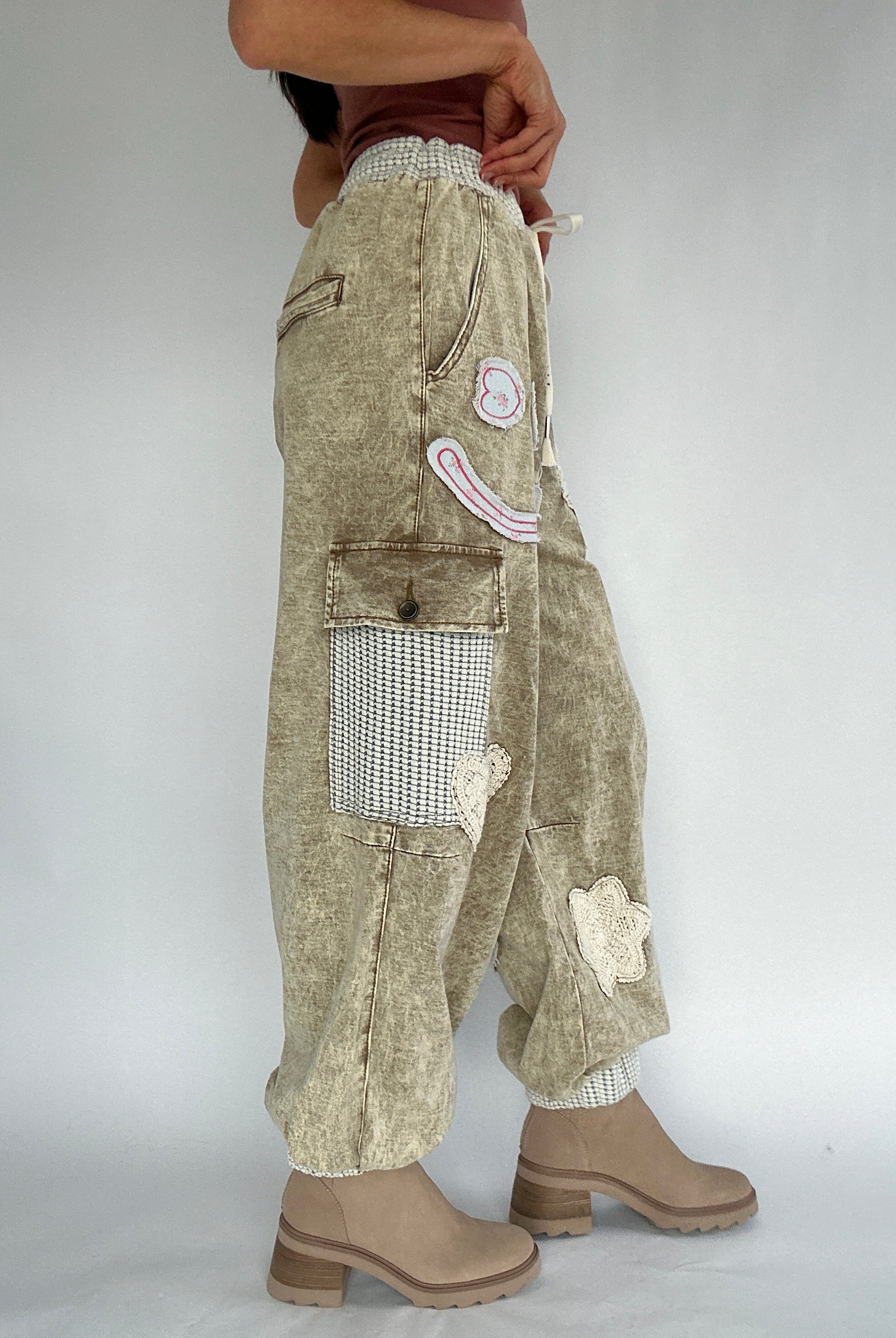 Person wearing beige patchwork jogger pants with a plain background from side