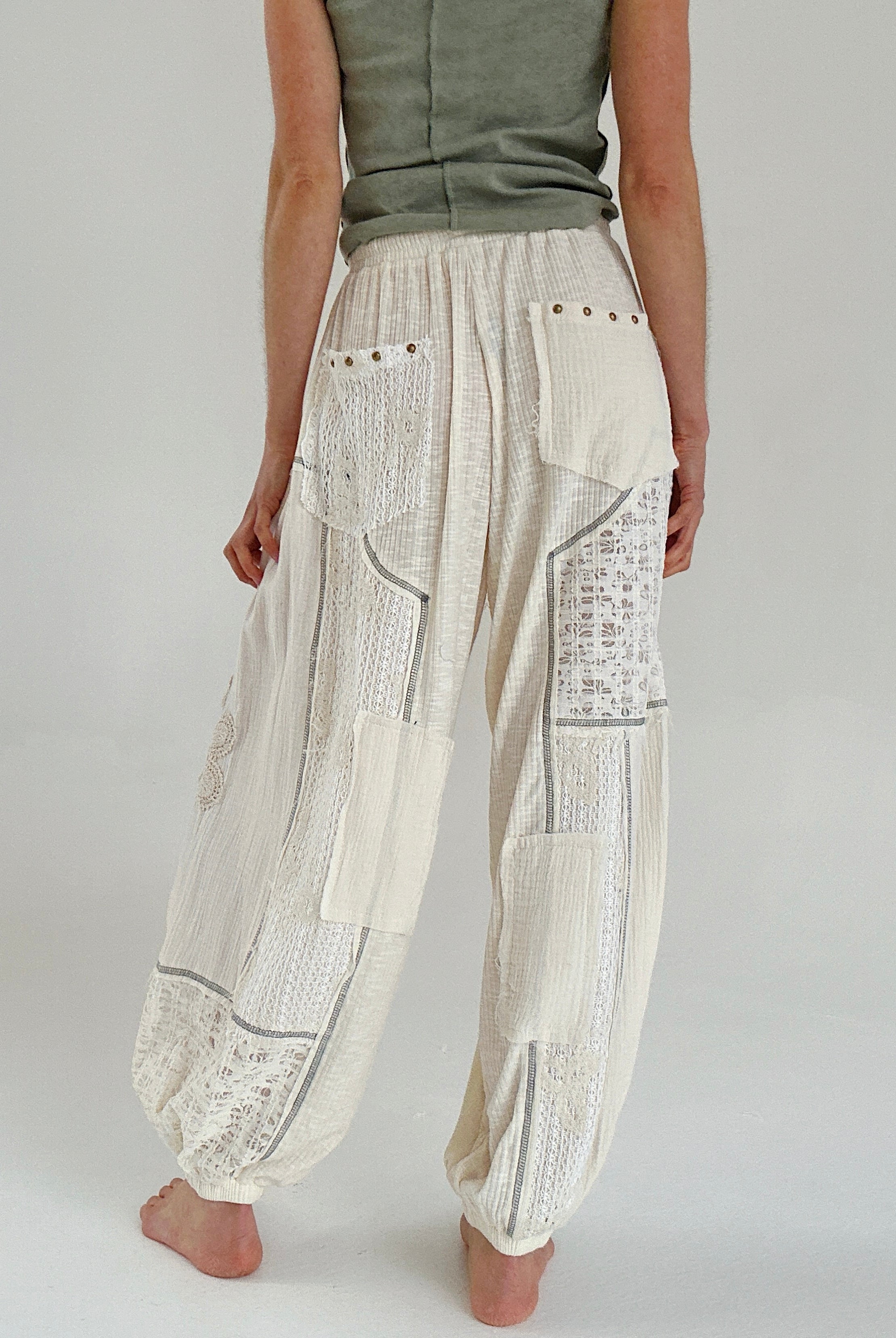Person wearing cream patchwork pants on a plain background showing back pocket details