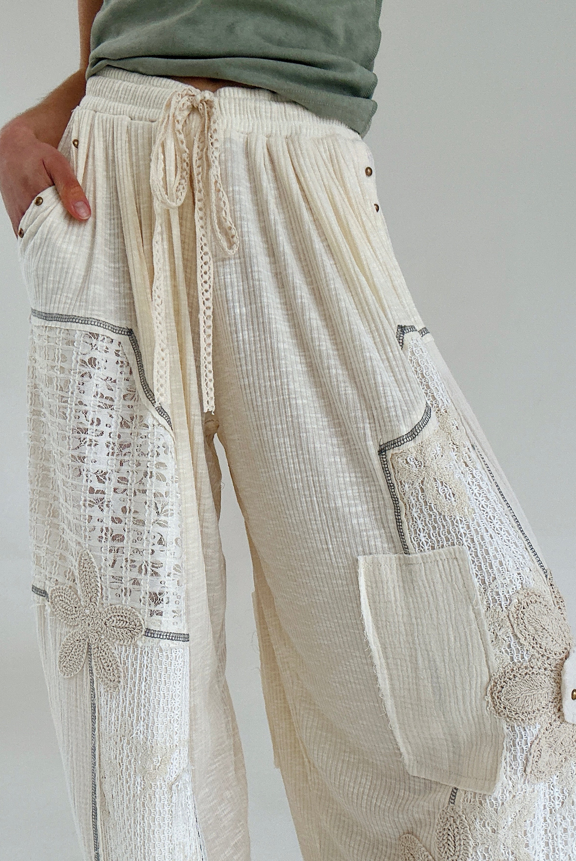 Beige wide-leg pants with lace details and an elastic drawstring waist on a plain background