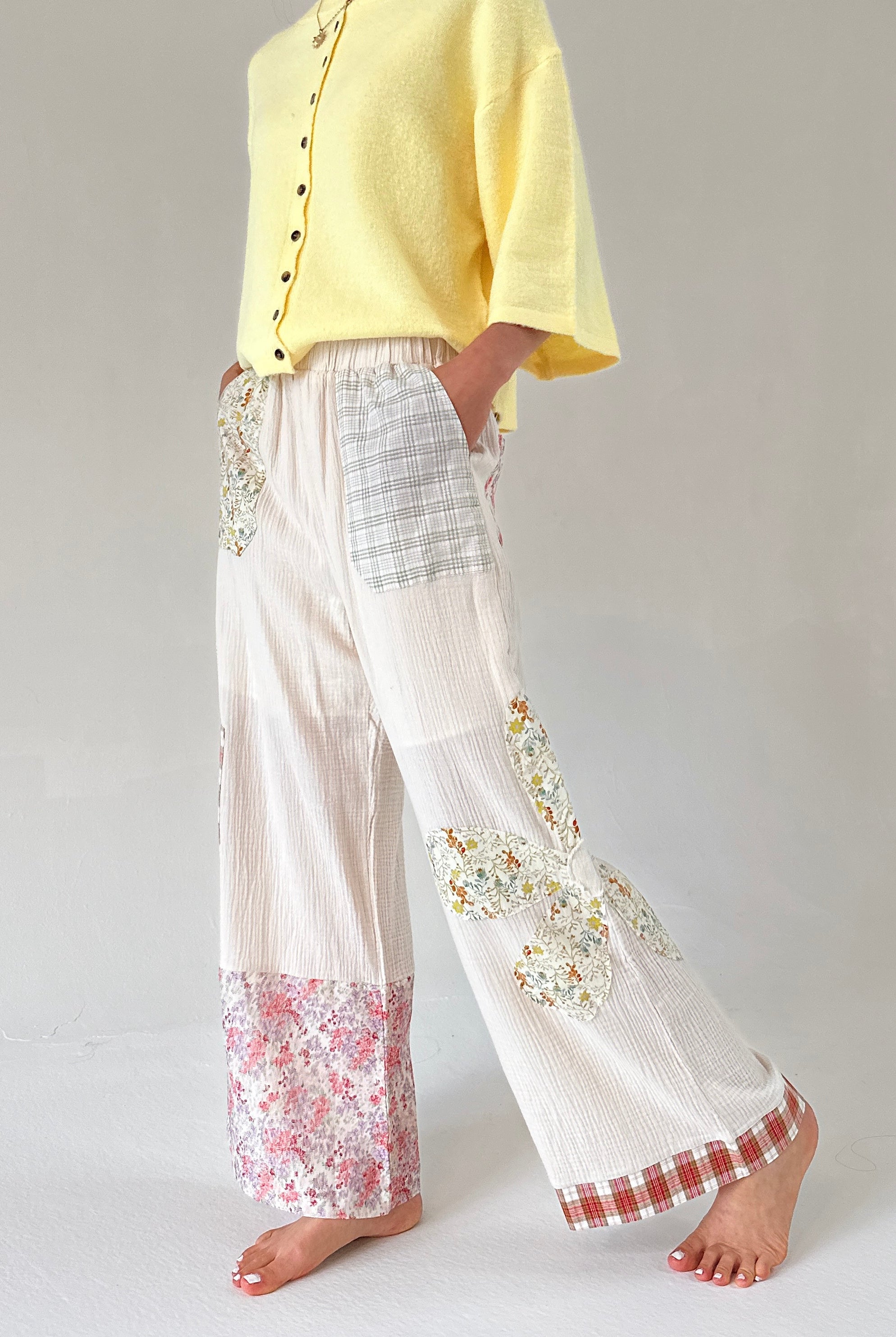 Person wearing a yellow top and white pants with floral and checkered patterns on a plain background