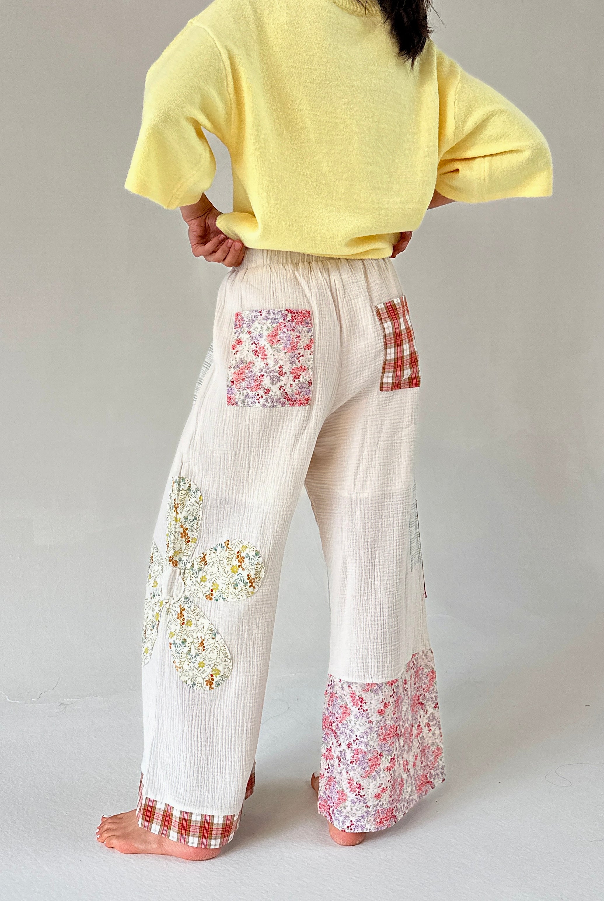 Person wearing a yellow top and floral patchwork pants on a plain background
