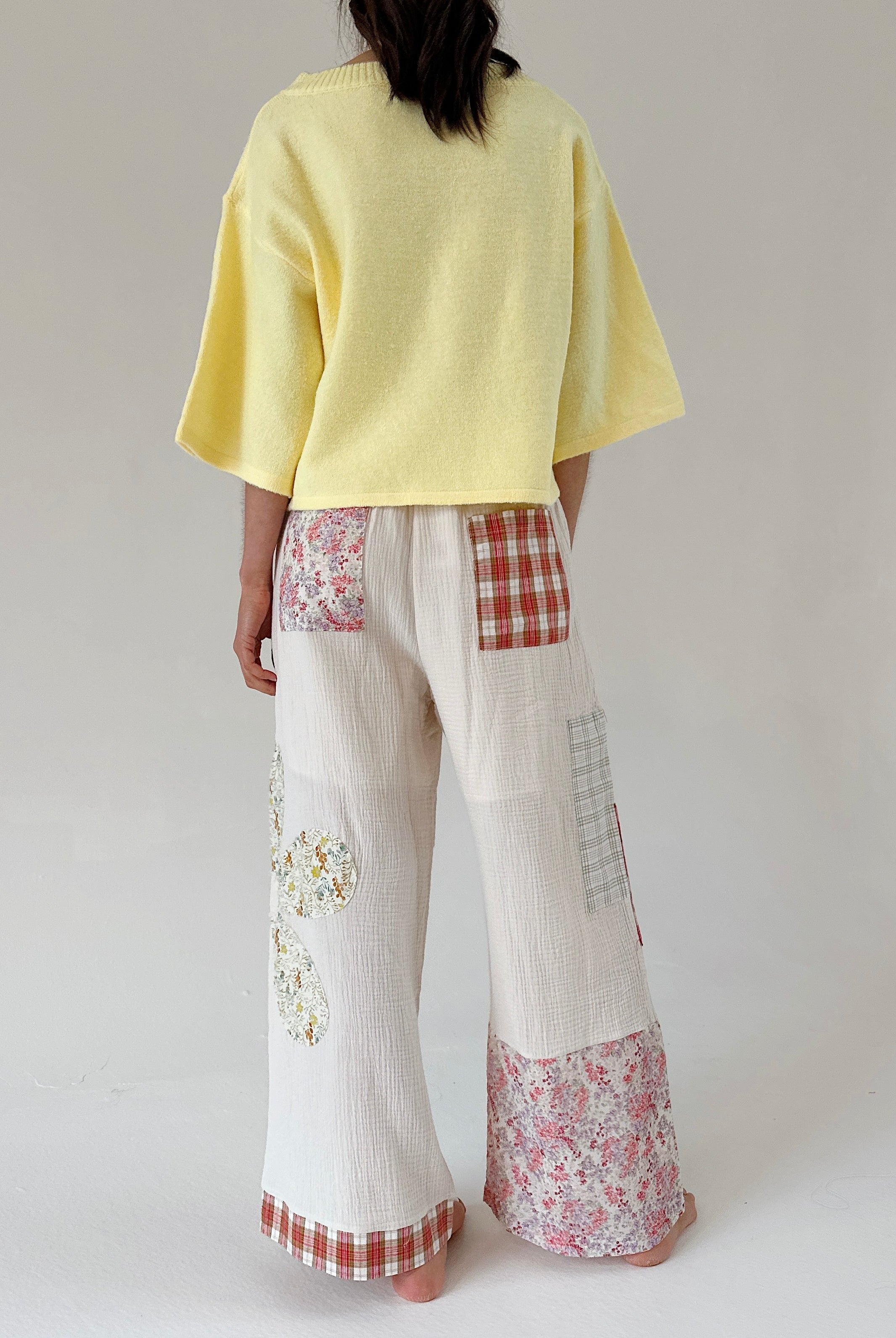 Person wearing a yellow top and patchwork pants on a plain background from back