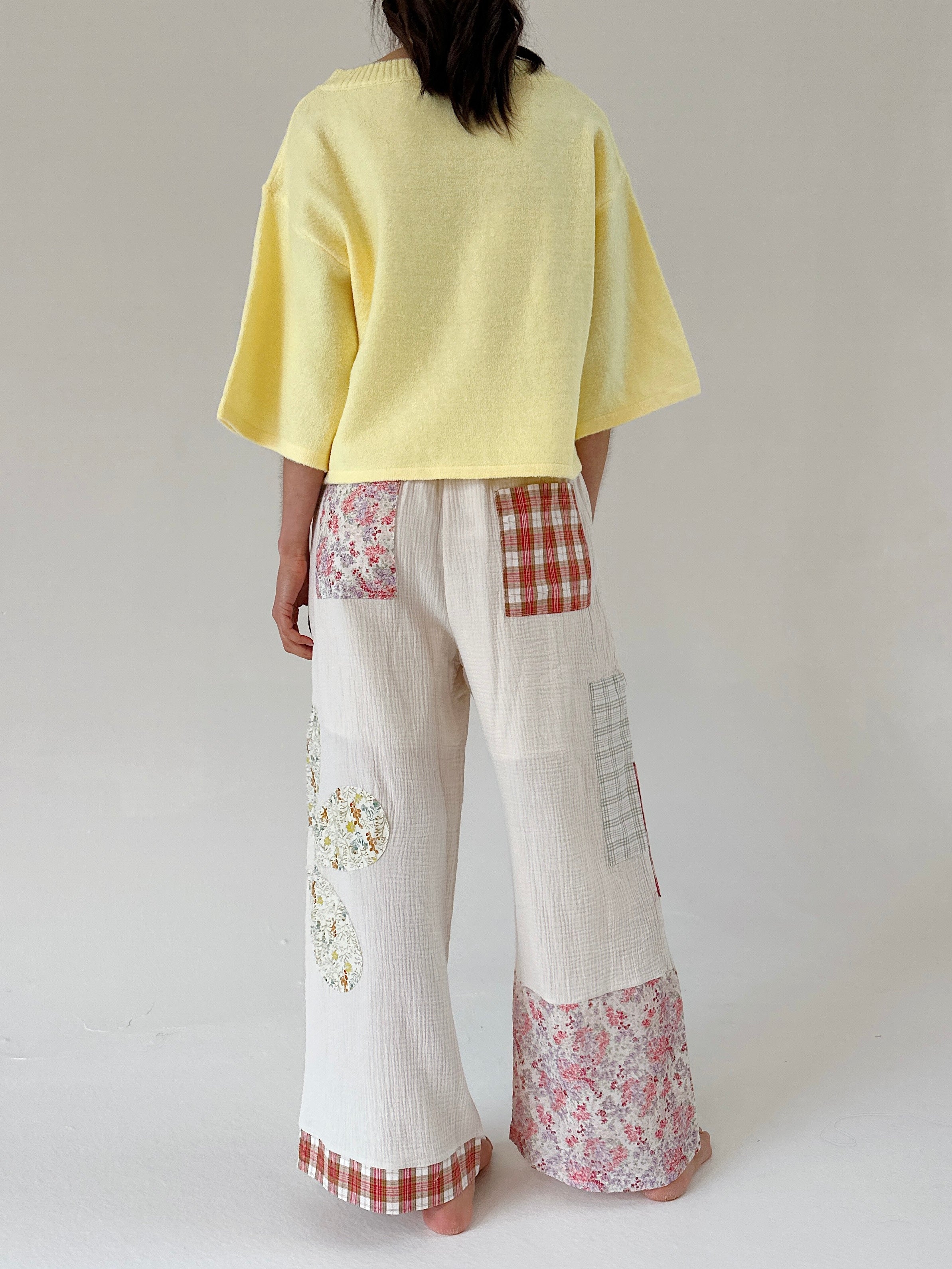Person wearing a yellow top and patchwork pants on a plain background from back