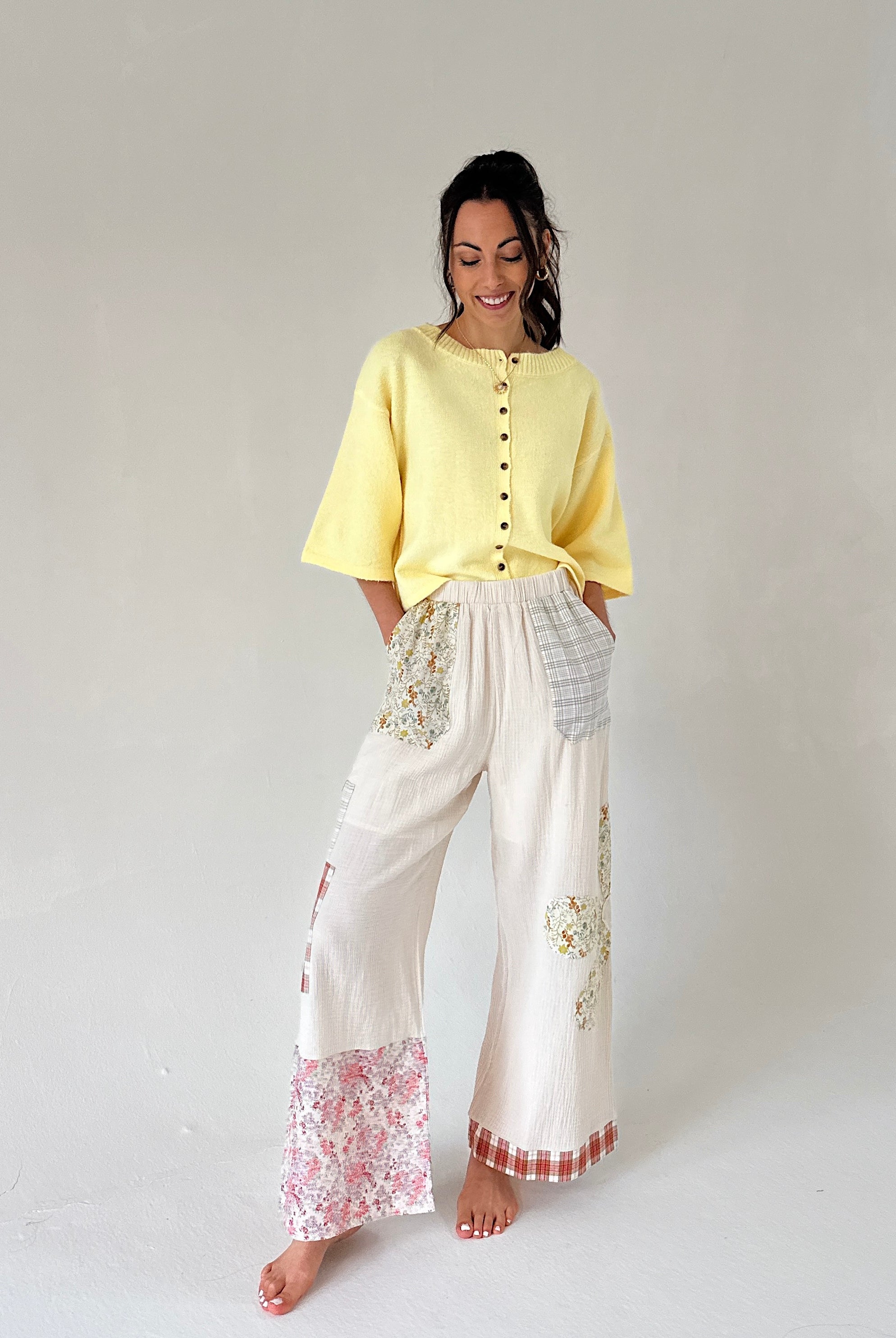 Woman wearing a yellow top and white pants with floral patterns on a plain background