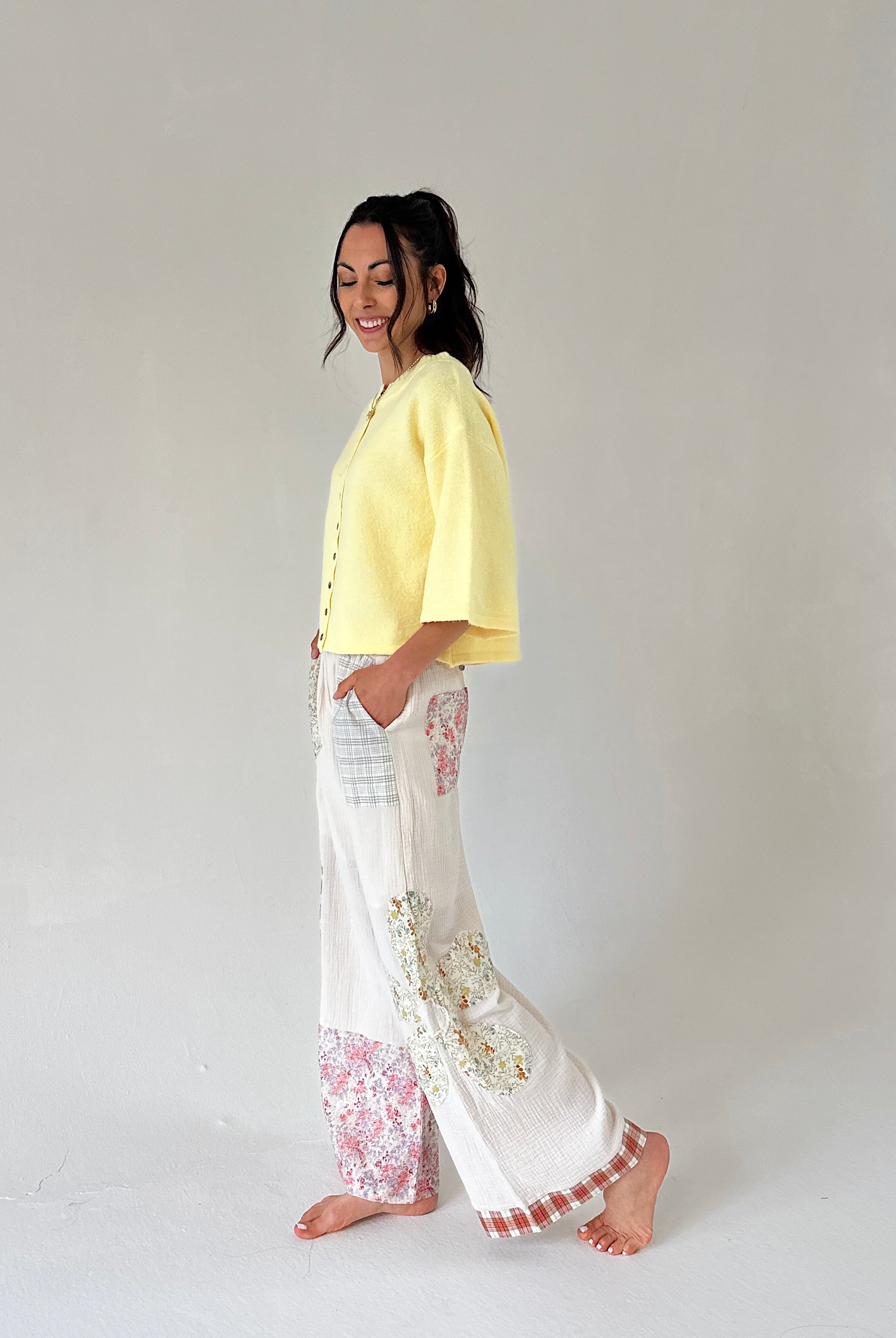Woman wearing a yellow top and white pants with floral patterns on a plain background