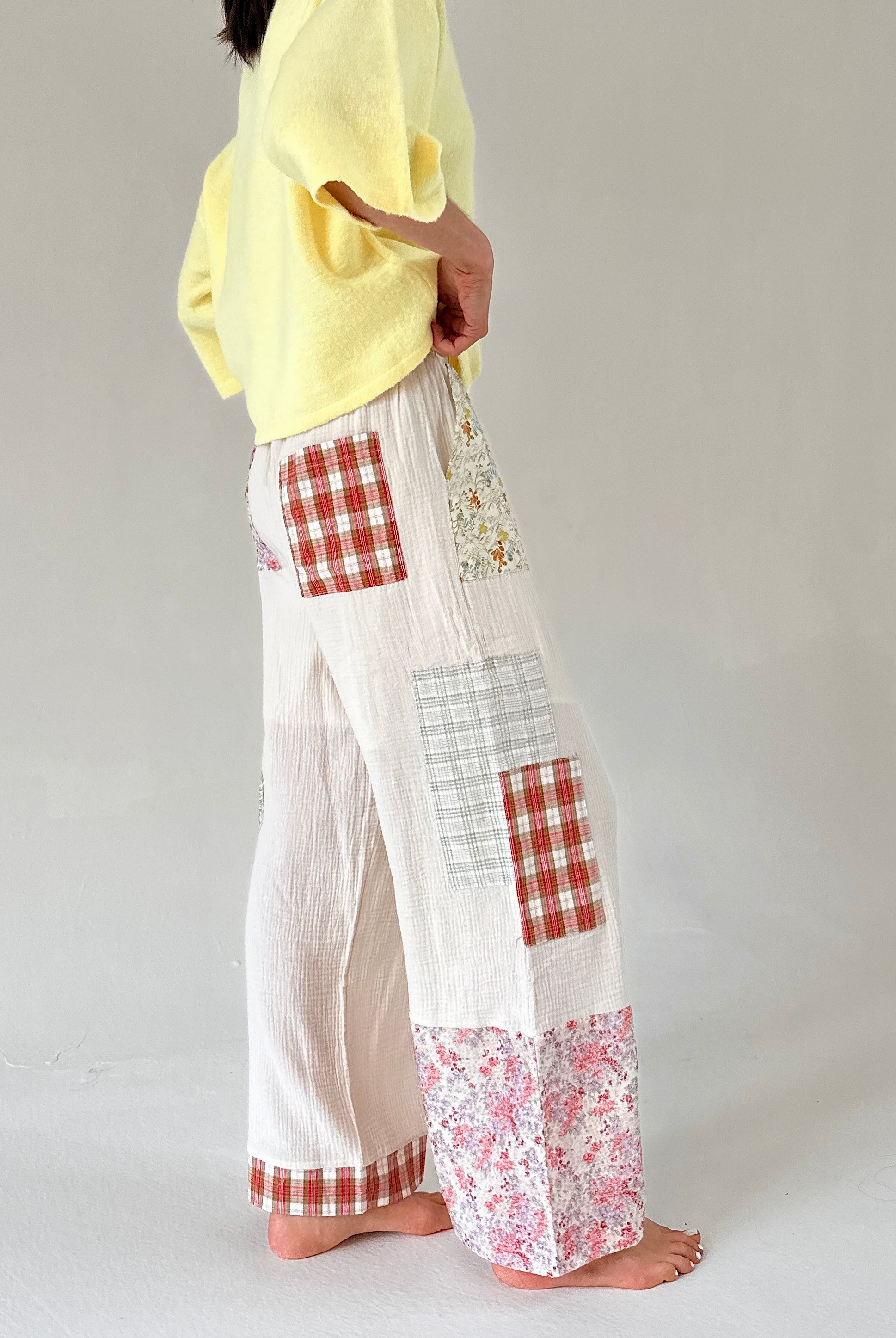 Person wearing a yellow top and white pants with red and white checkered and floral patches on a plain background from side