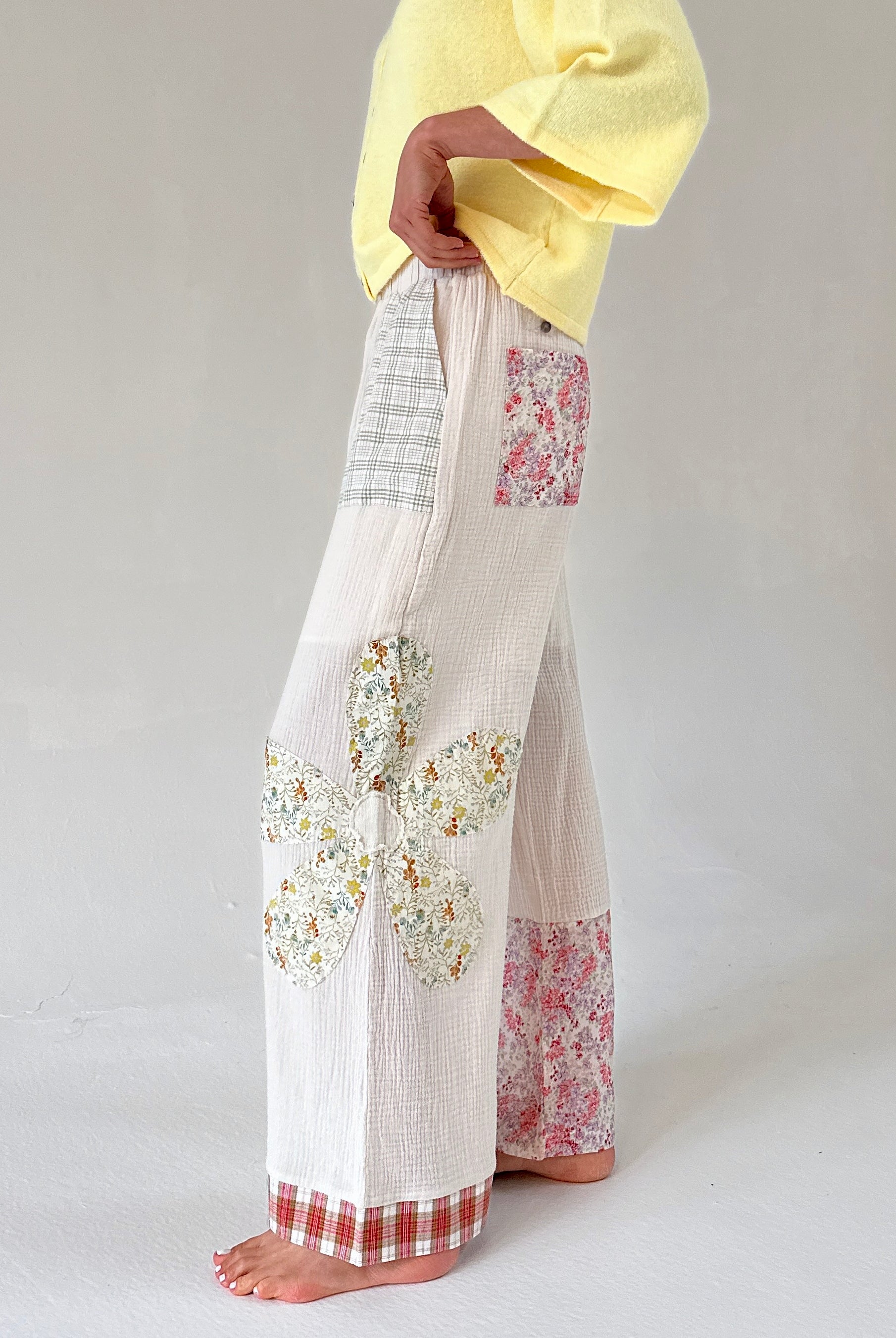 Person wearing white pants with floral patterns on a plain background from side