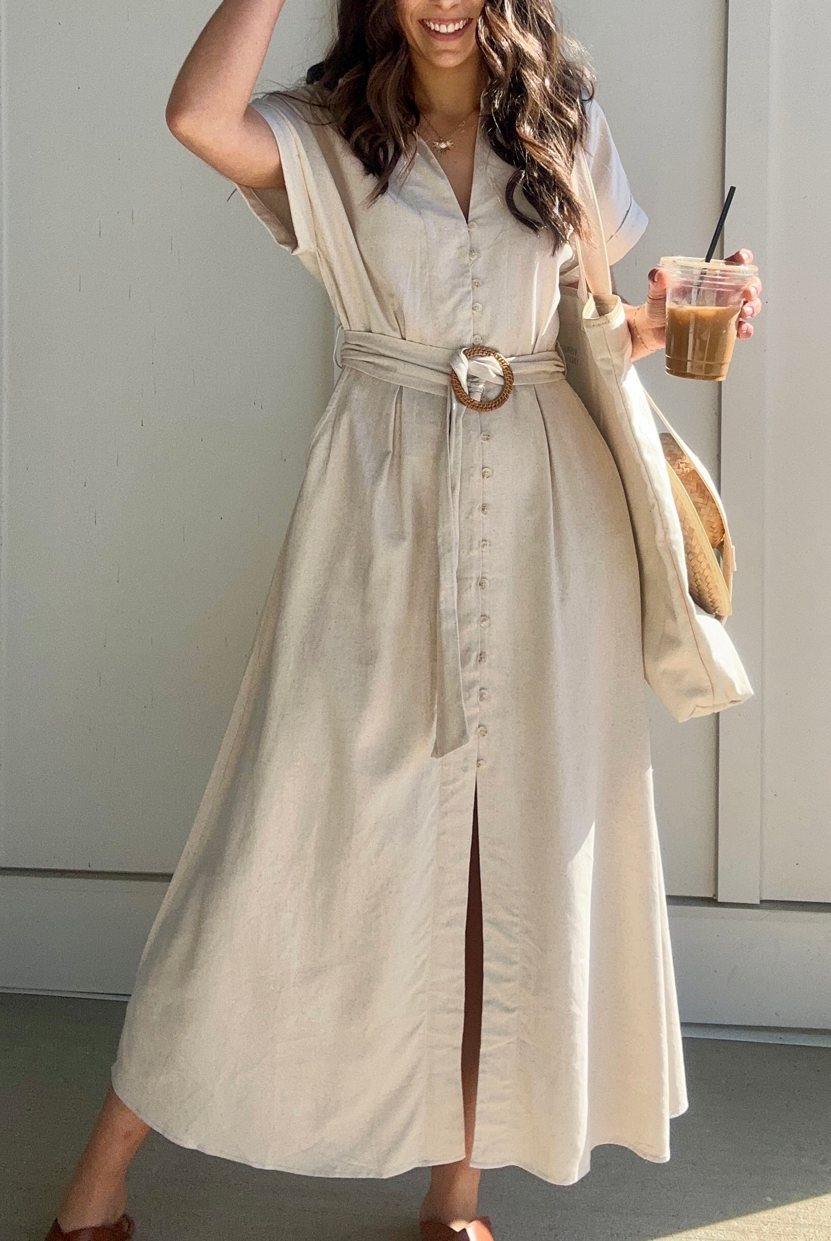 Oatmeal linen maxi dress with button down front and waist belt. Woman is holding a coffee.