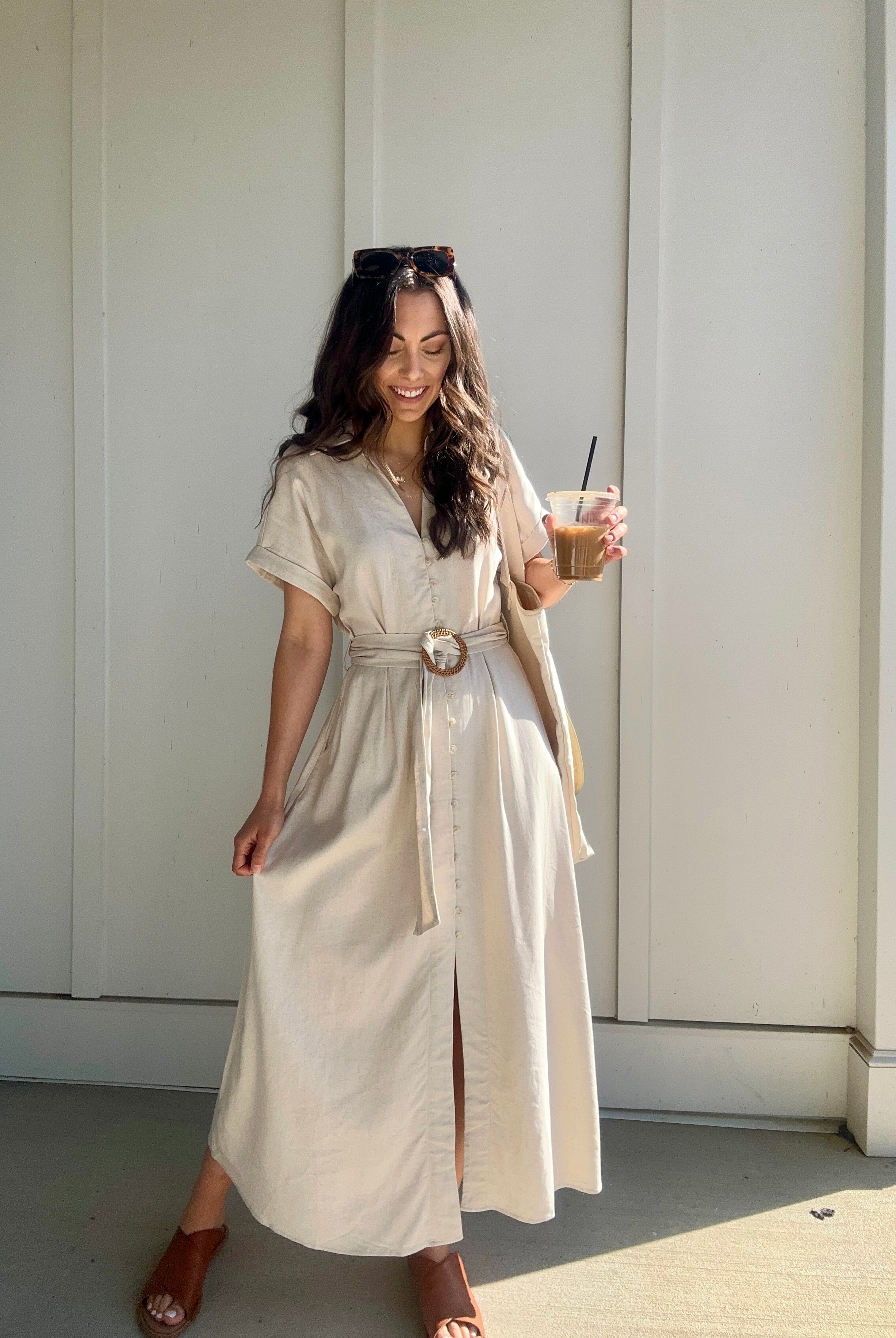 woman wearing oatmeal linen dress with waist belt and is holding a coffee