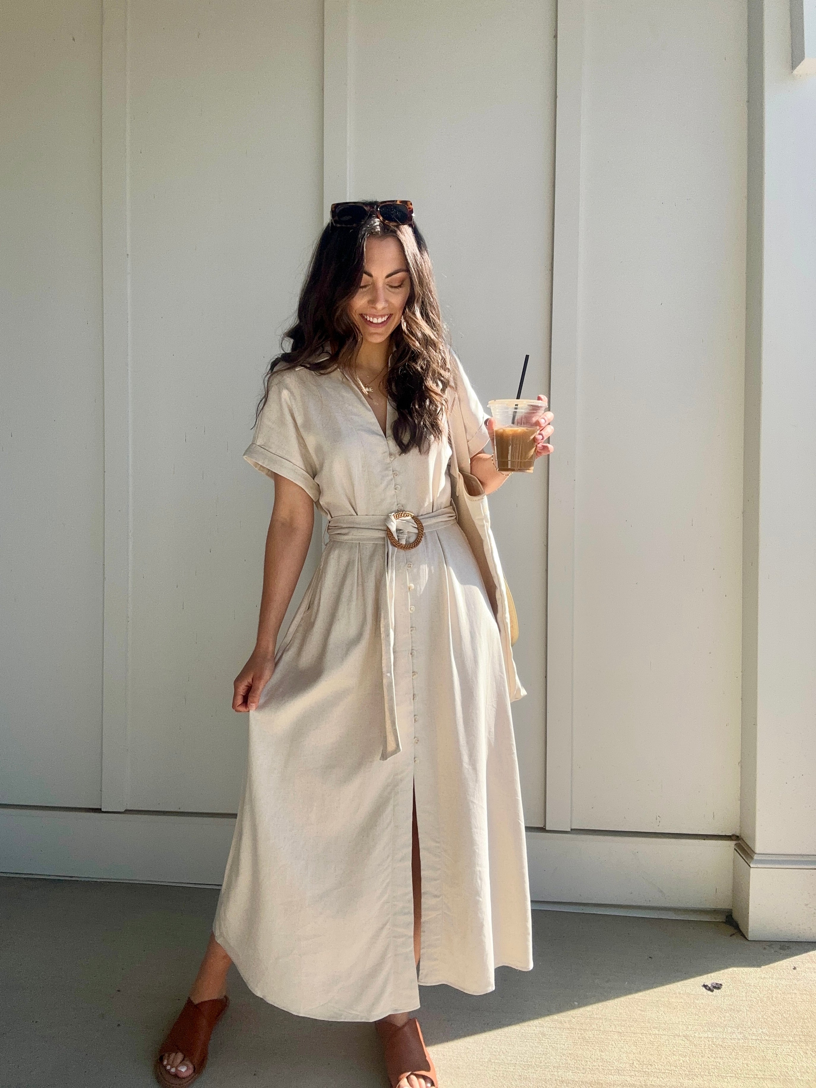woman wearing oatmeal linen dress with waist belt and is holding a coffee