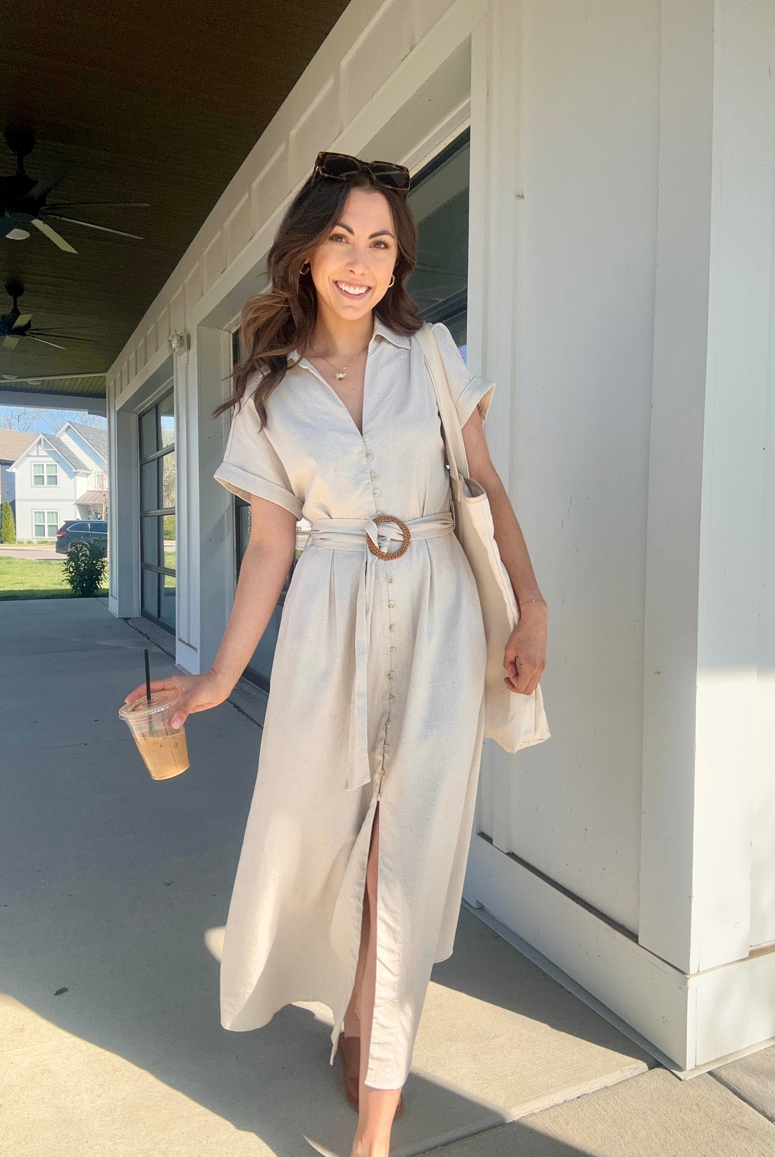 Woman wearing an oatmeal linen maxi dress with button front and waist belt, carrying a coffee.