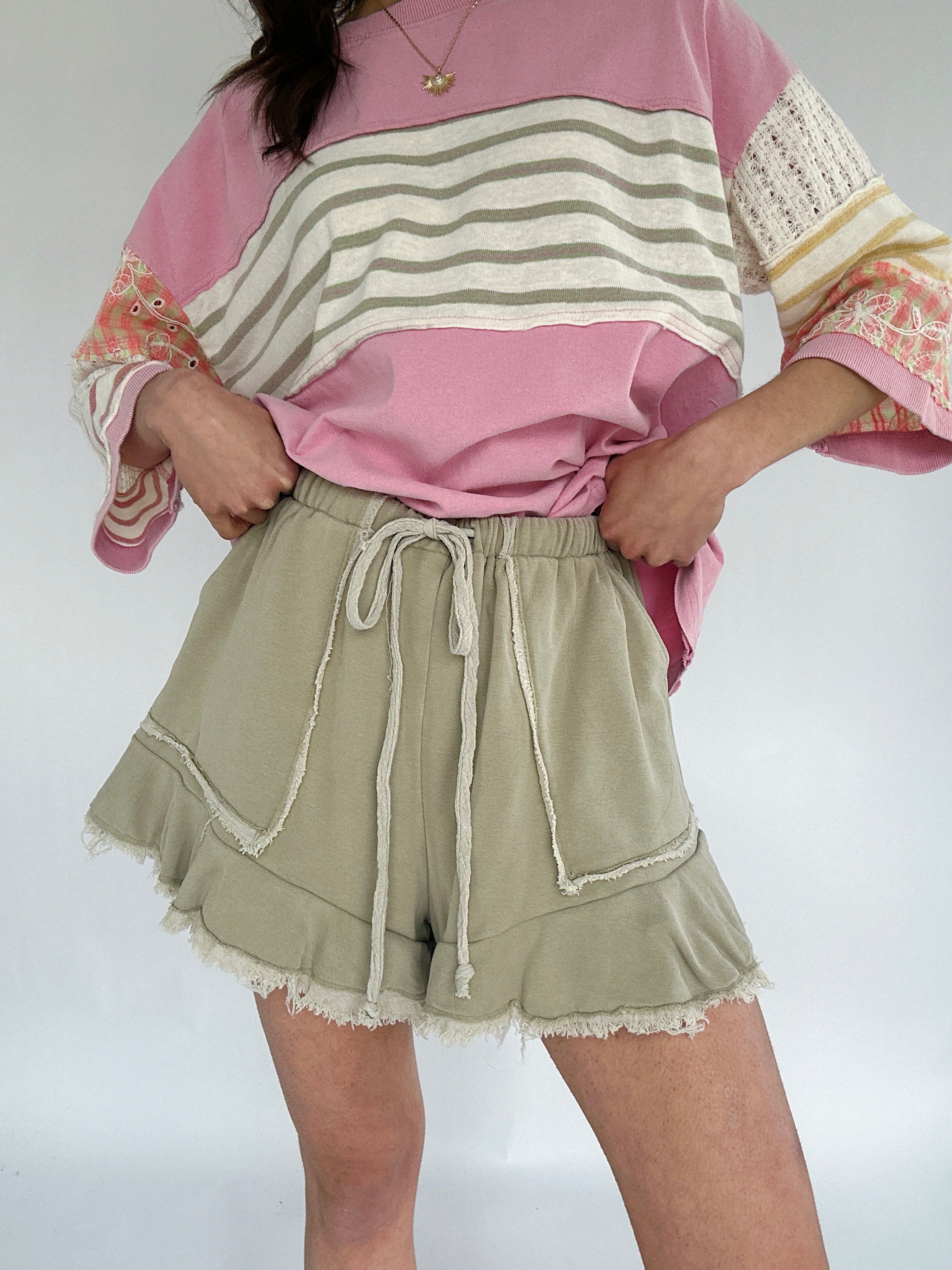 Person wearing a pink and striped long-sleeve top with olive green shorts on a white background