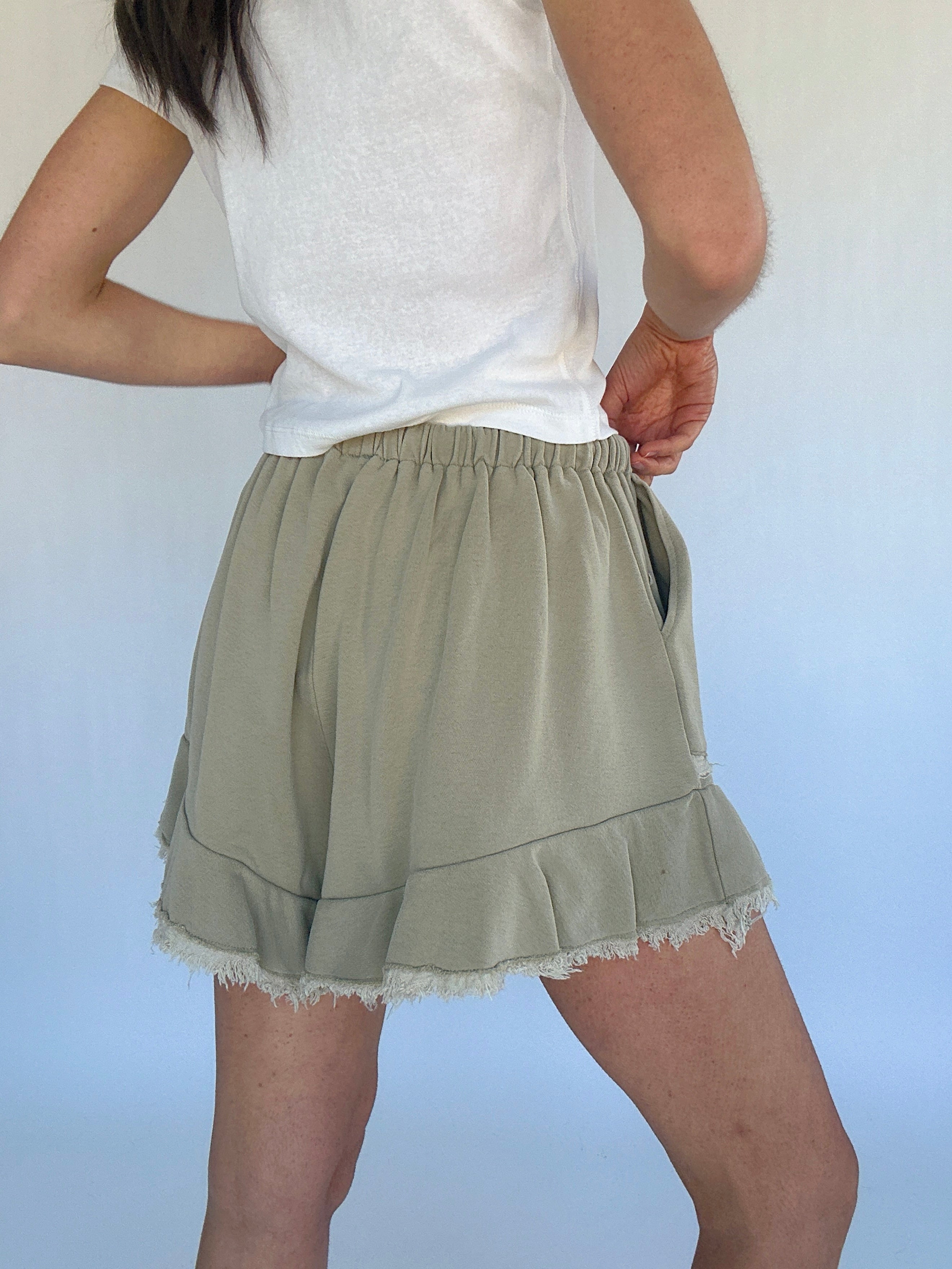 Person wearing a white top and olive green shorts against a plain background