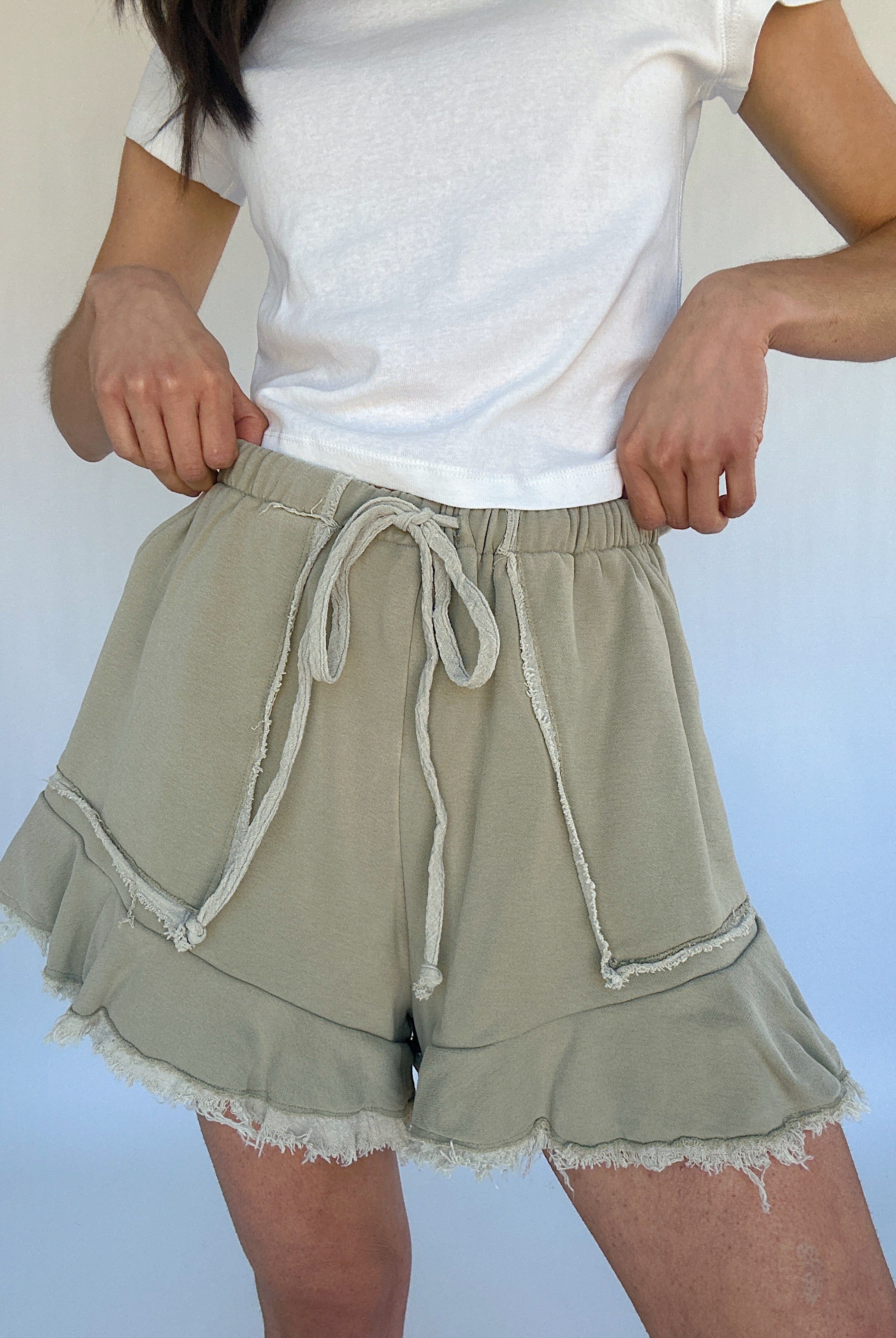 Person wearing a white t-shirt and light green shorts with ruffled hem on a plain background