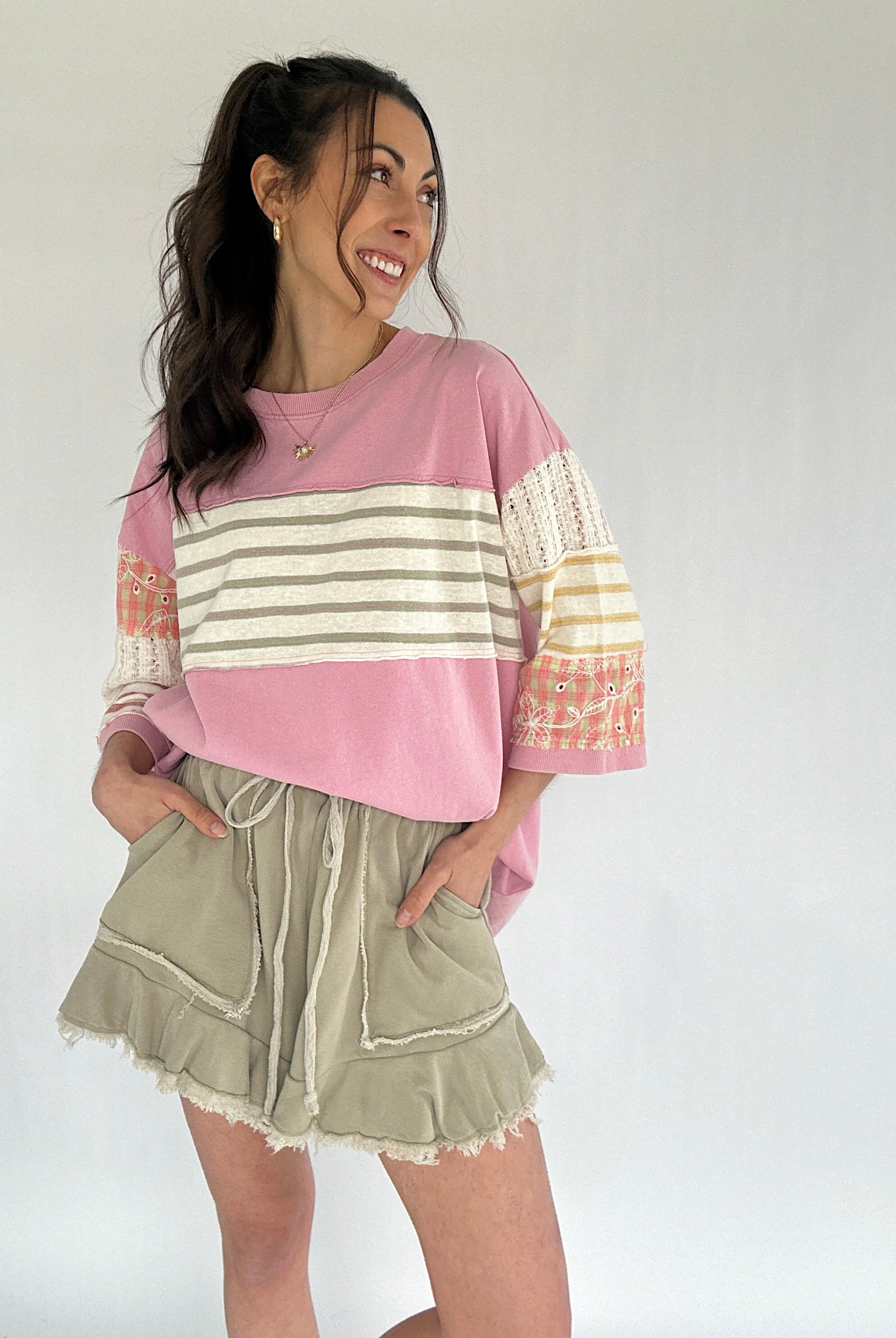 Woman wearing a pink and beige striped sweater with olive green shorts on a white background