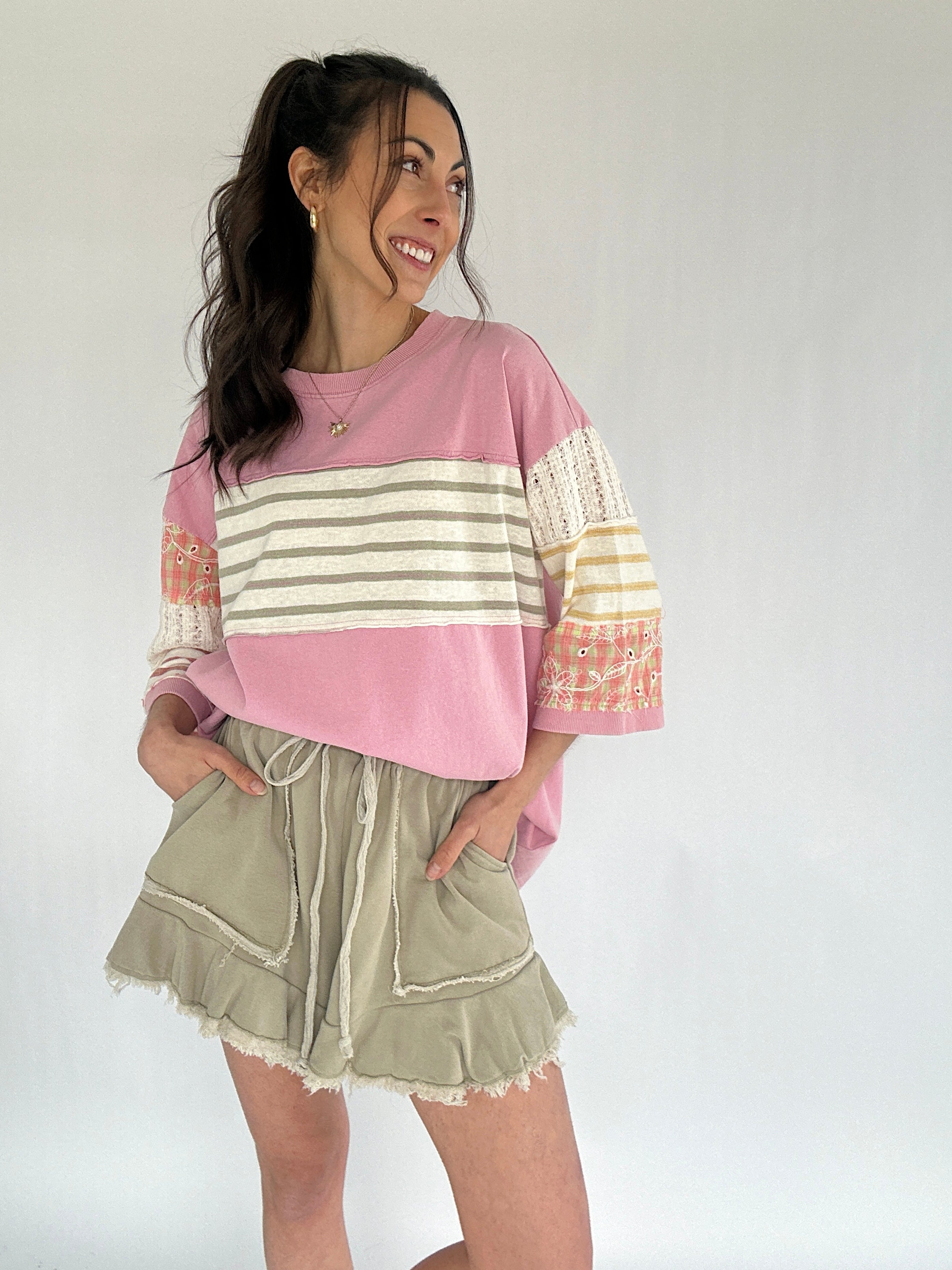 Woman wearing a pink and beige striped sweater with olive green shorts on a white background
