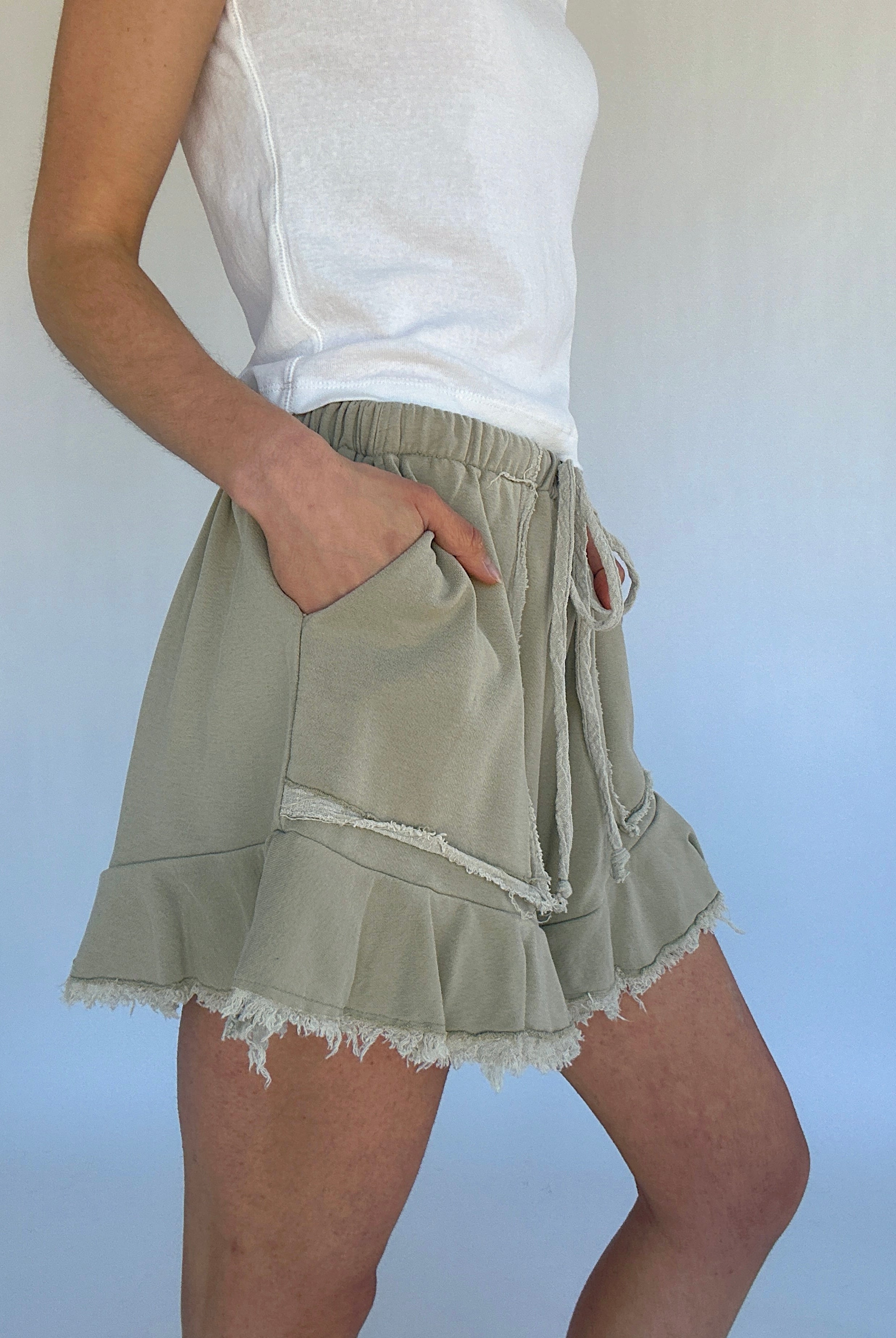 Person wearing light green shorts with a white top against a plain background showing side pockets