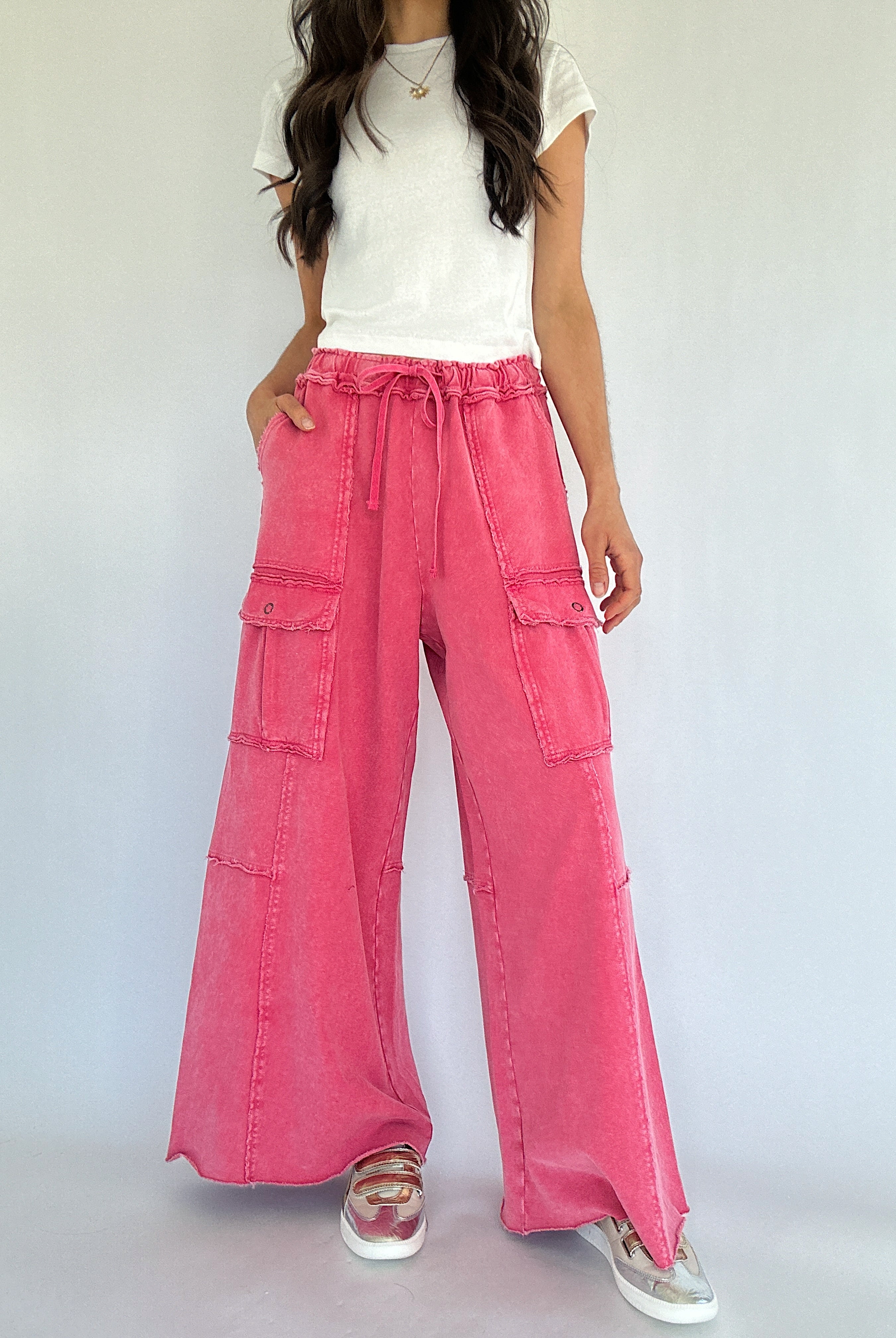 Person wearing pink wide-leg pants with cargo pockets and a white top on a plain background