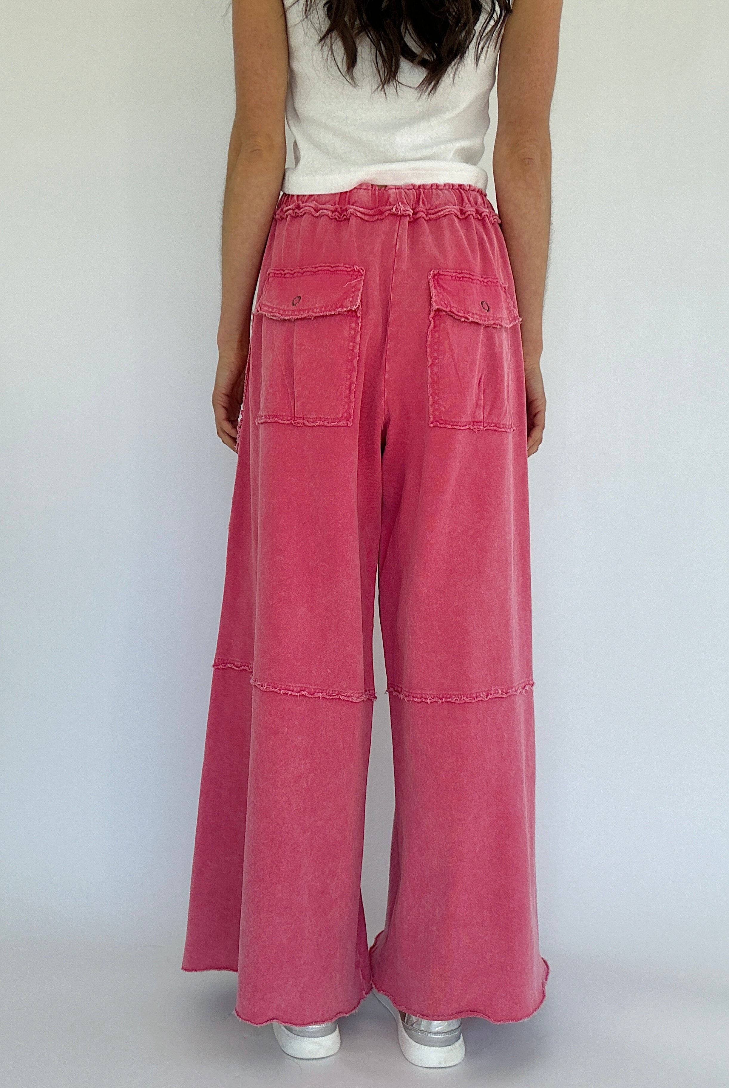 Person wearing pink wide-leg pants and a white top on a plain background showing the back