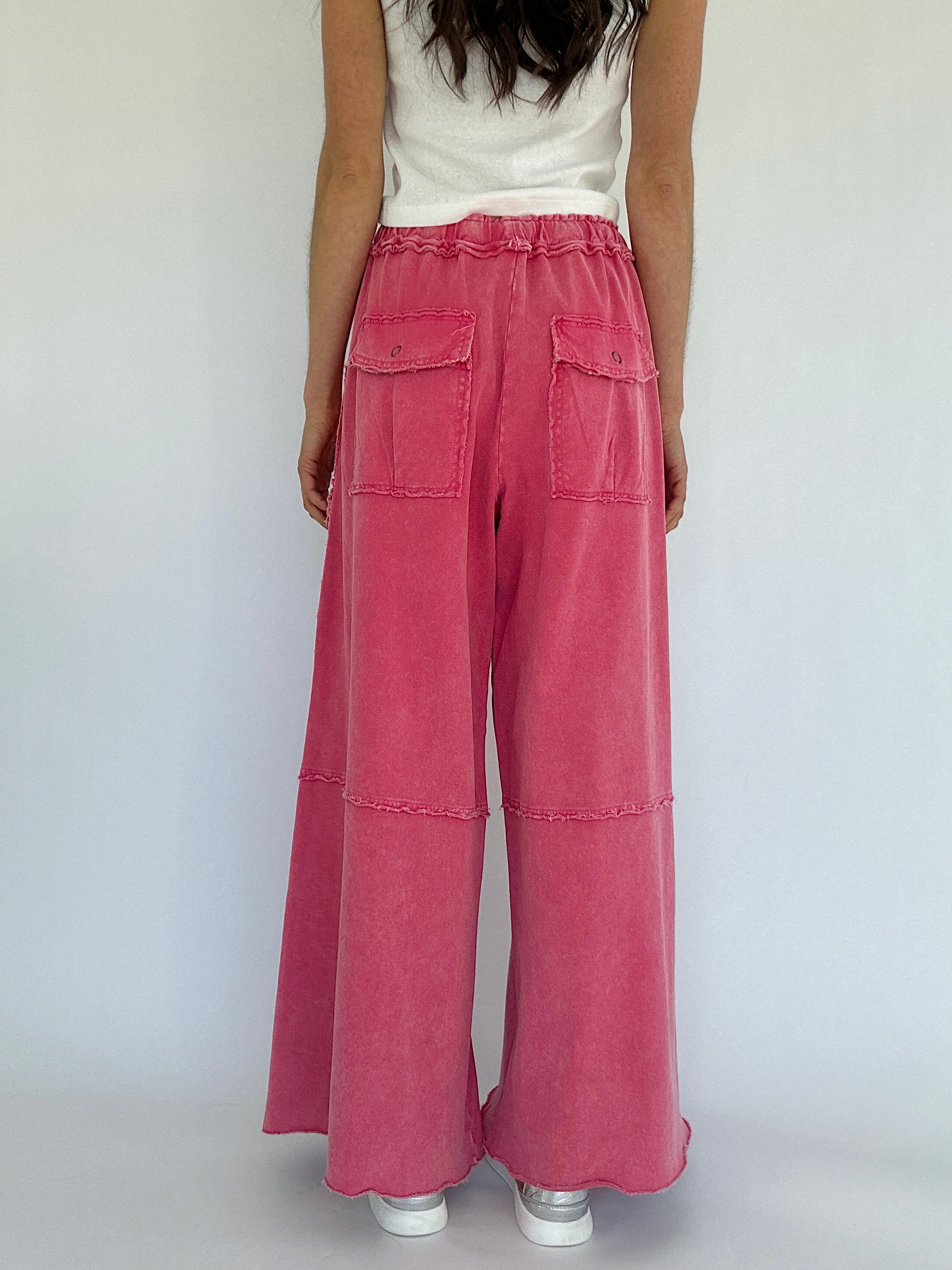 Person wearing pink wide-leg pants and a white top on a plain background showing the back