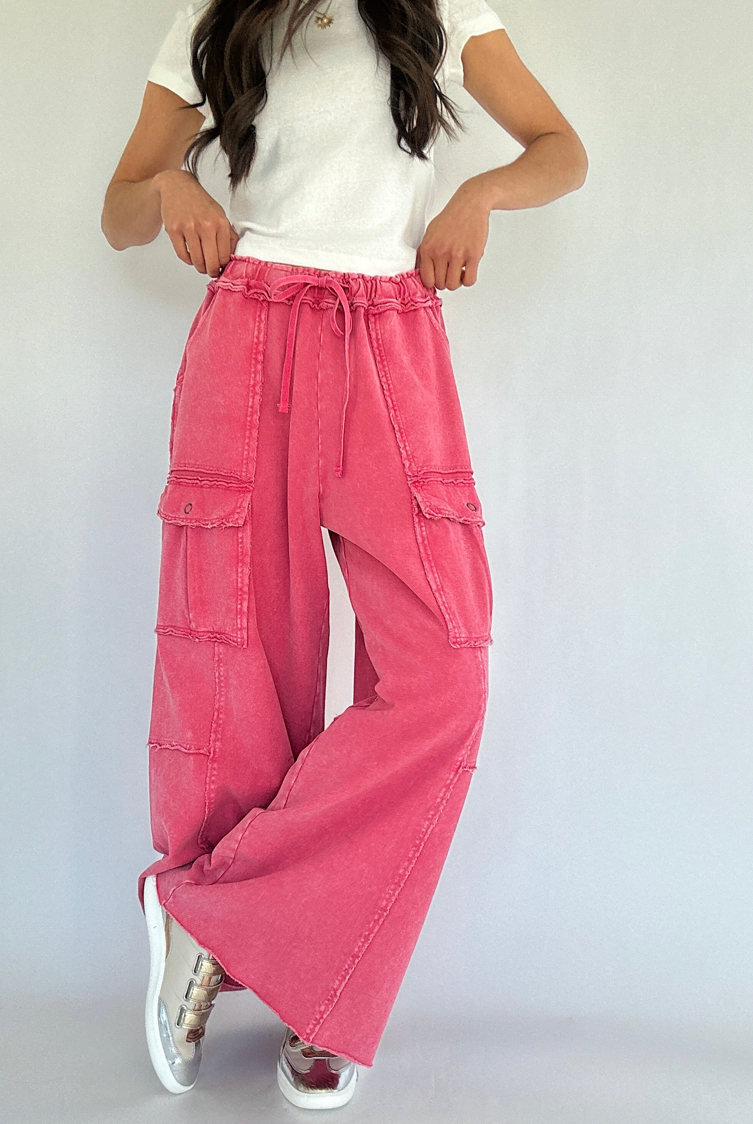 Person wearing pink cargo pants and a white top on a plain background