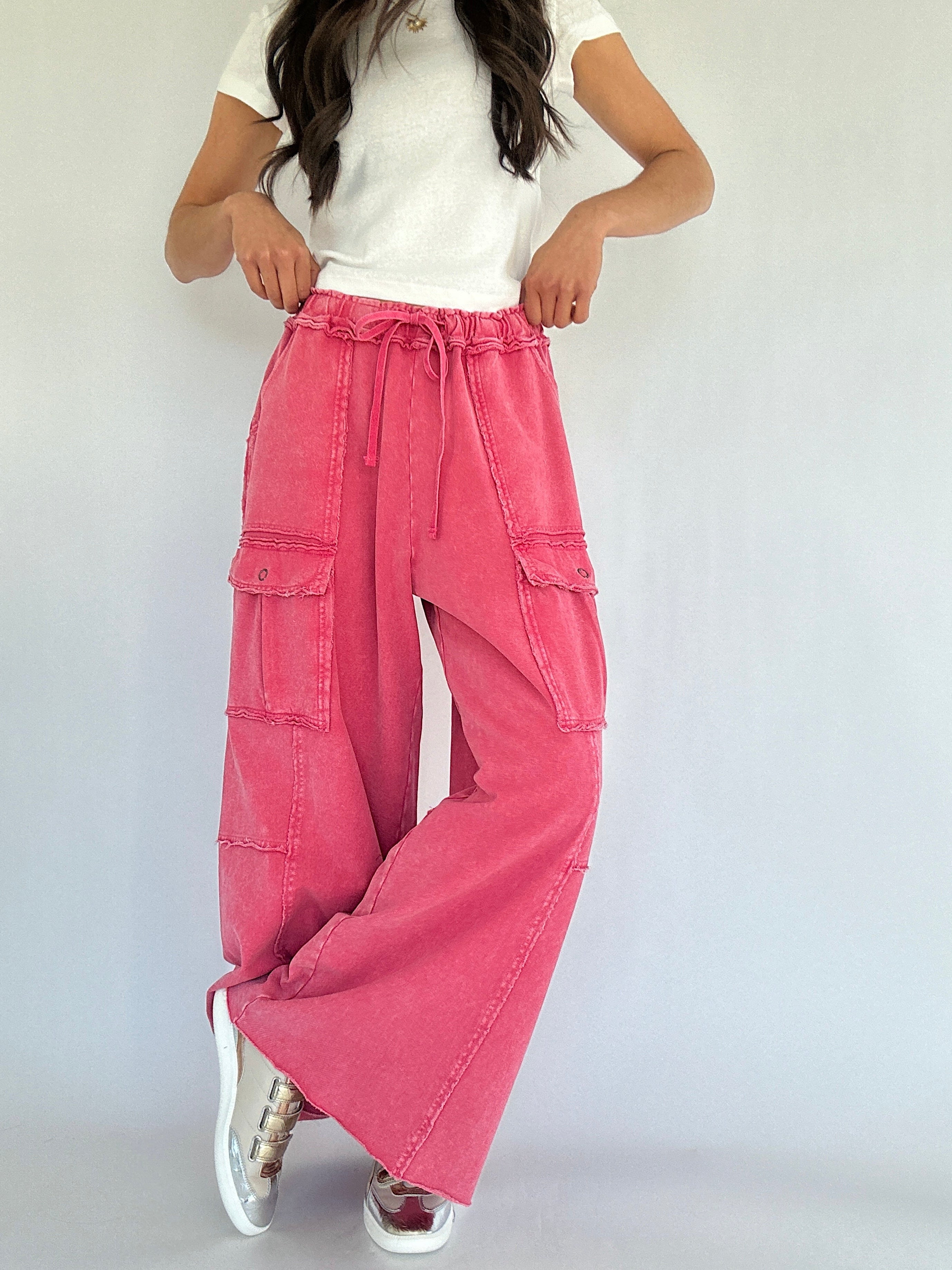 Person wearing pink cargo pants and a white top on a plain background