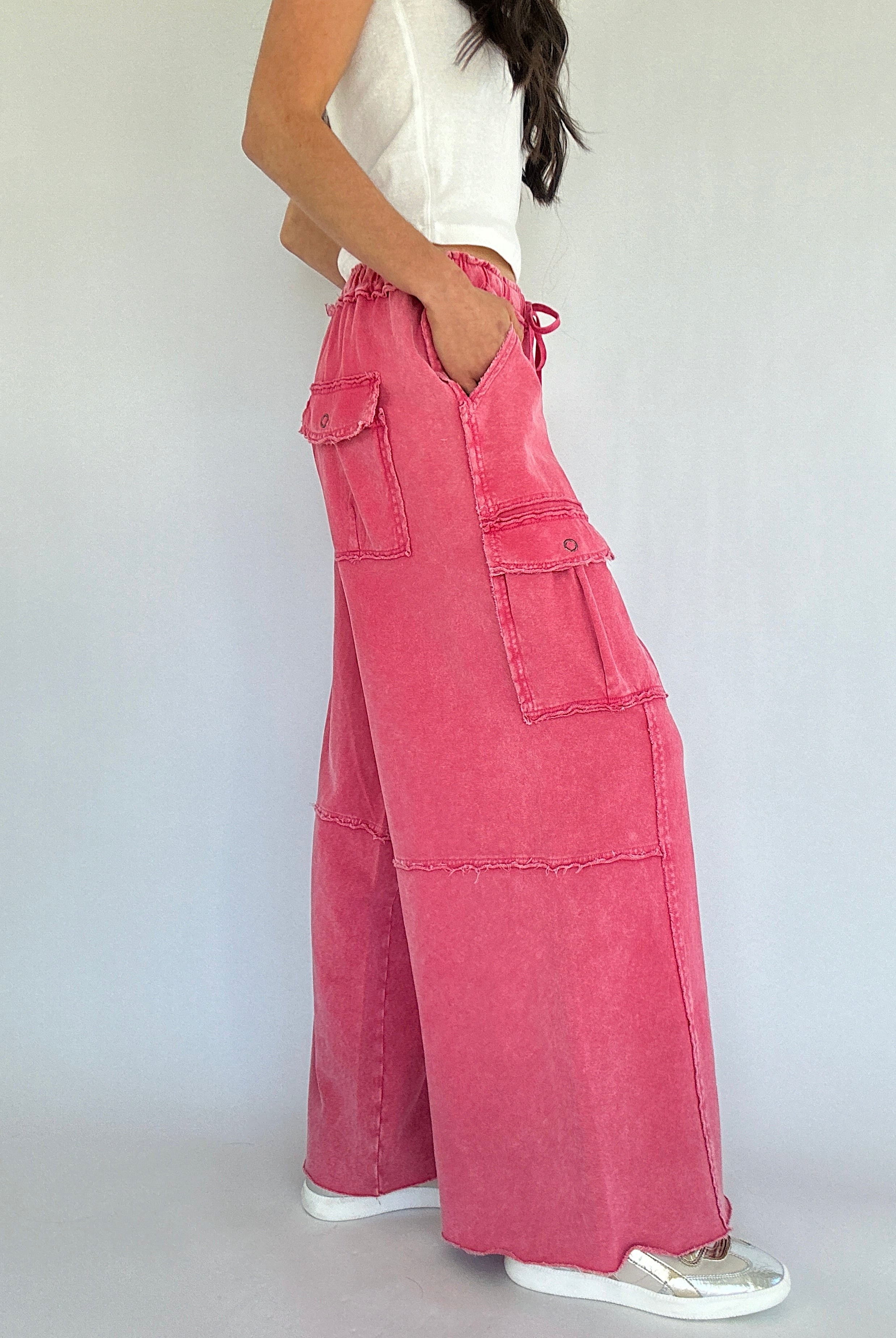 Person wearing pink wide-leg pants with a white top on a plain background showing the side