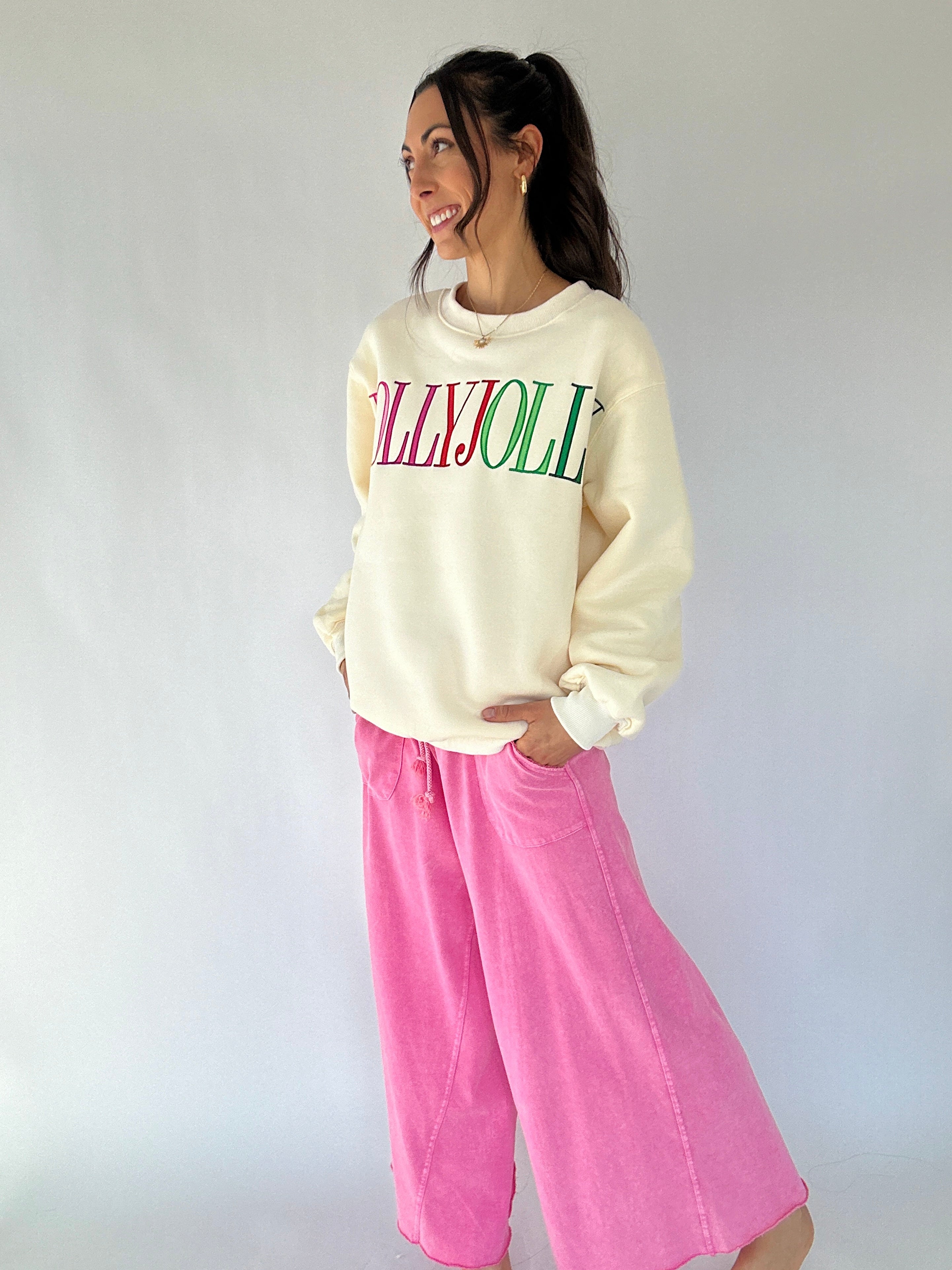 Woman wearing a cream sweatshirt with colorful text and pink pants against a white background