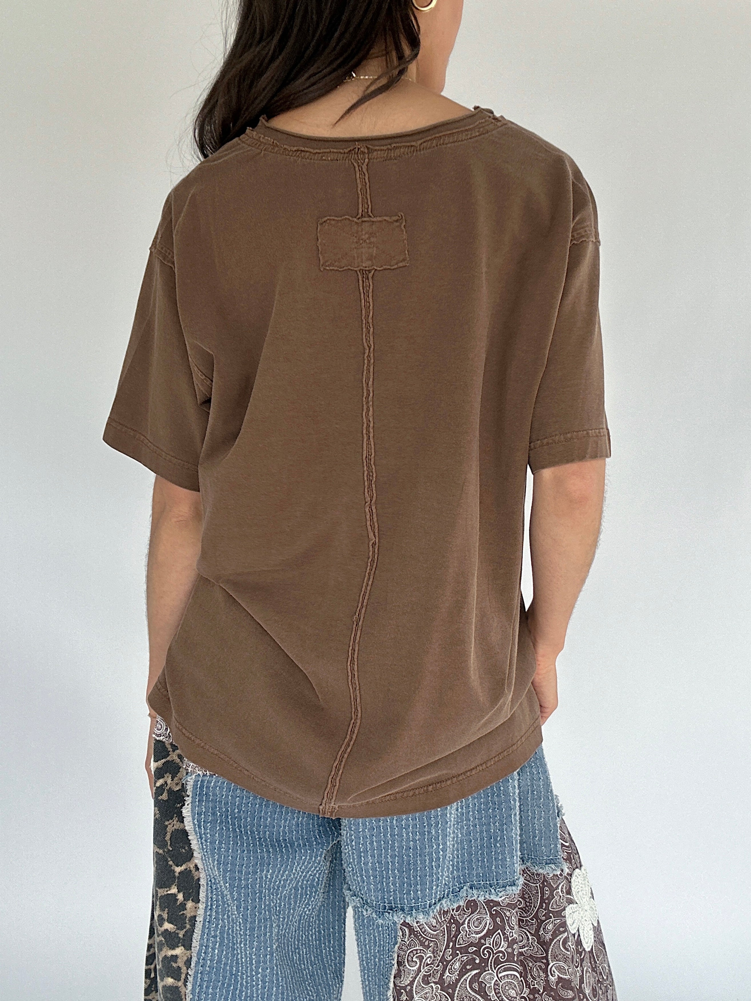 Person wearing a brown oversized t-shirt with a plain background showing back view