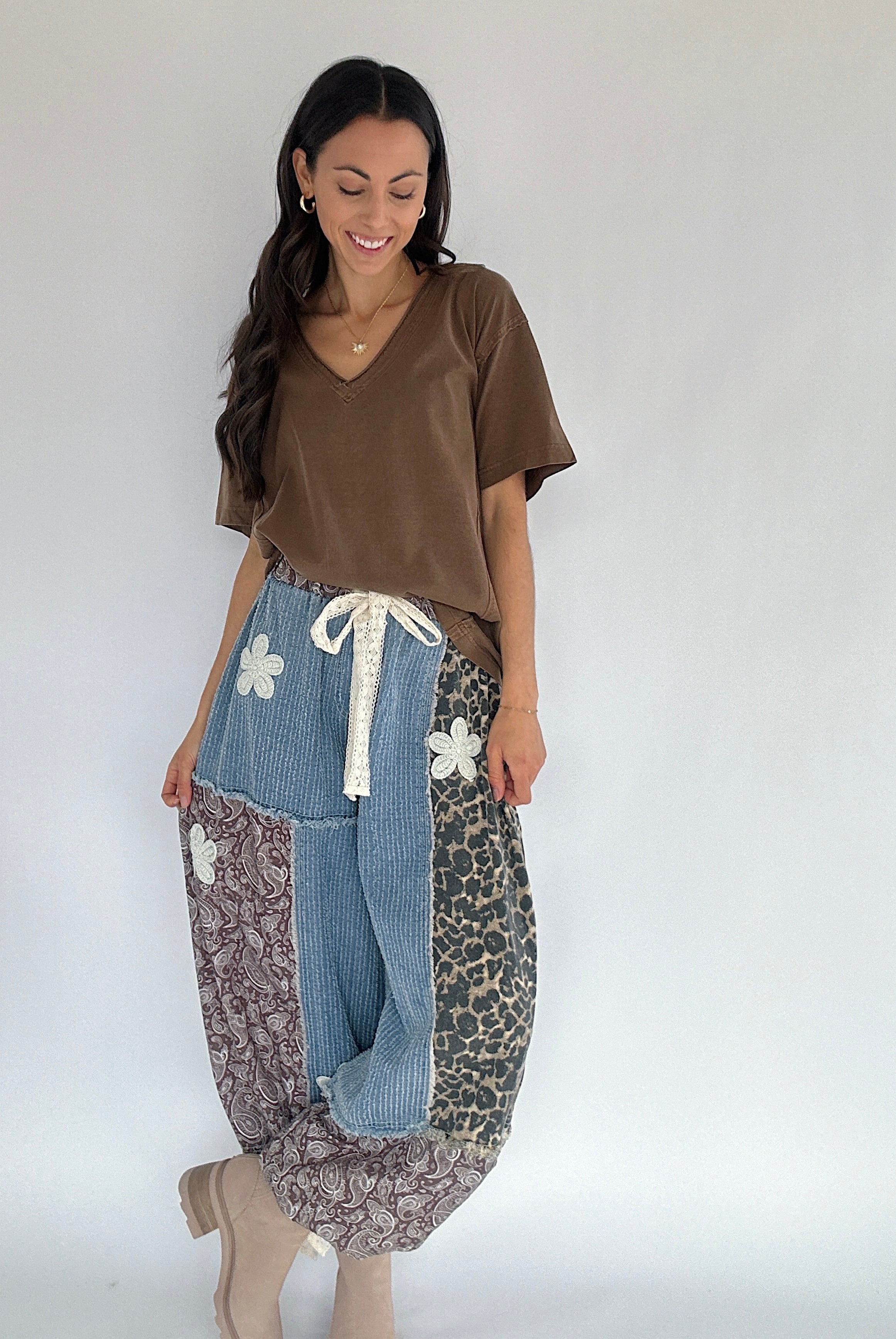 Woman wearing a brown tee tucked into patterned pants with denim accents on a plain background