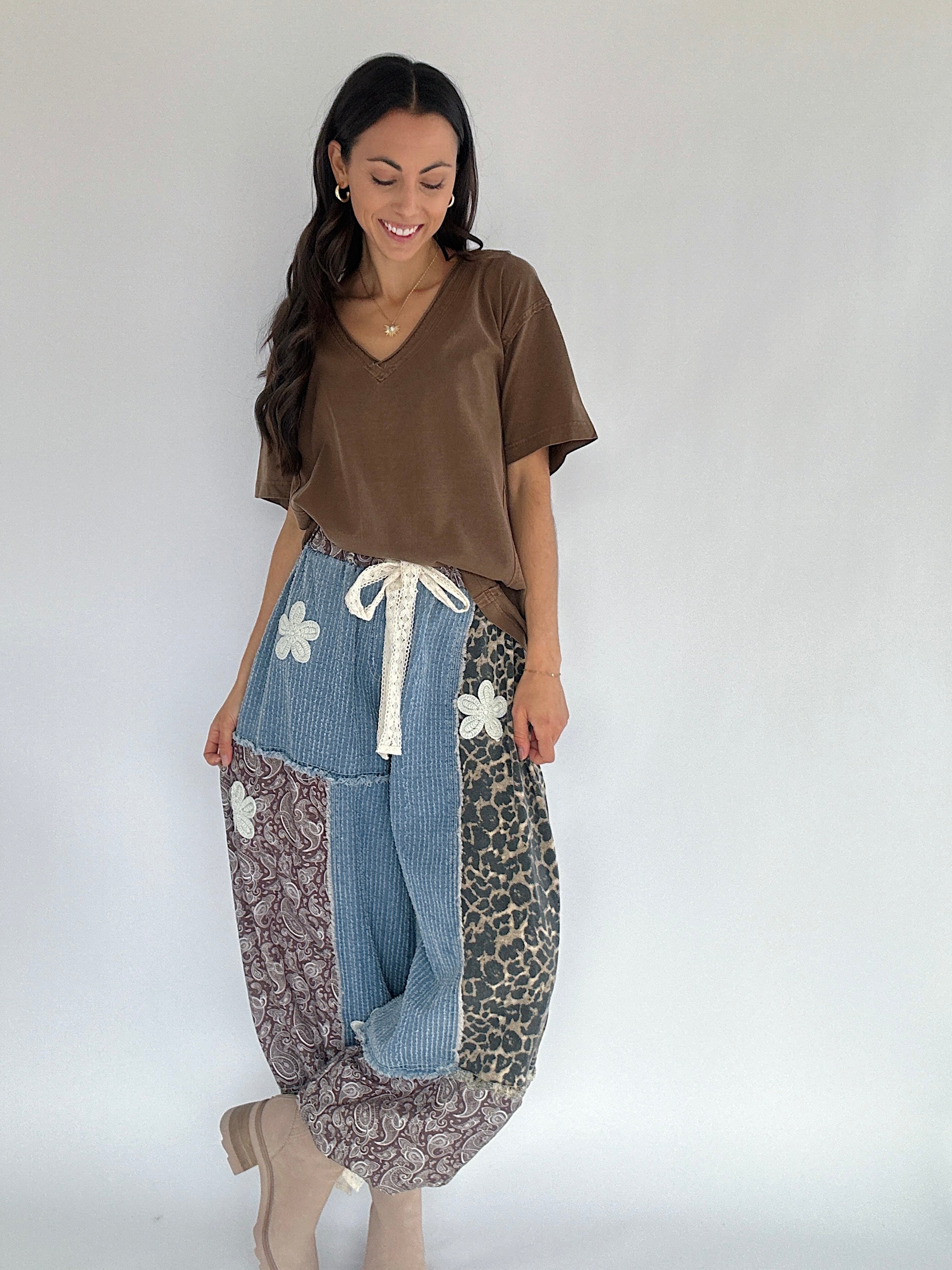 Woman wearing a brown tee tucked into patterned pants with denim accents on a plain background