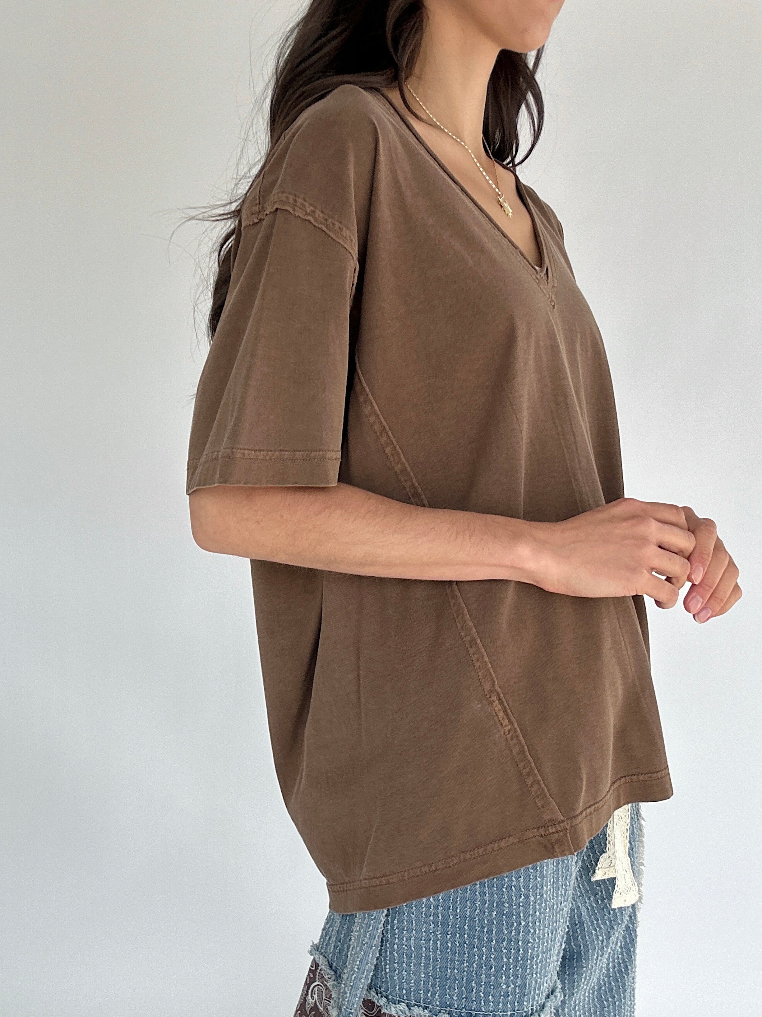 Person wearing a brown t-shirt with a plain background from side