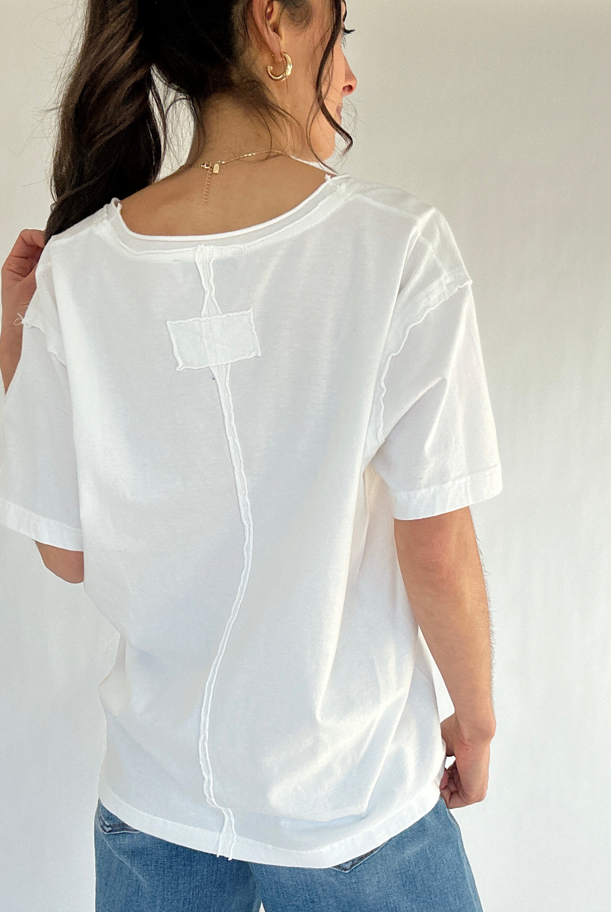 Person wearing a white tee with jeans from back with a plain background