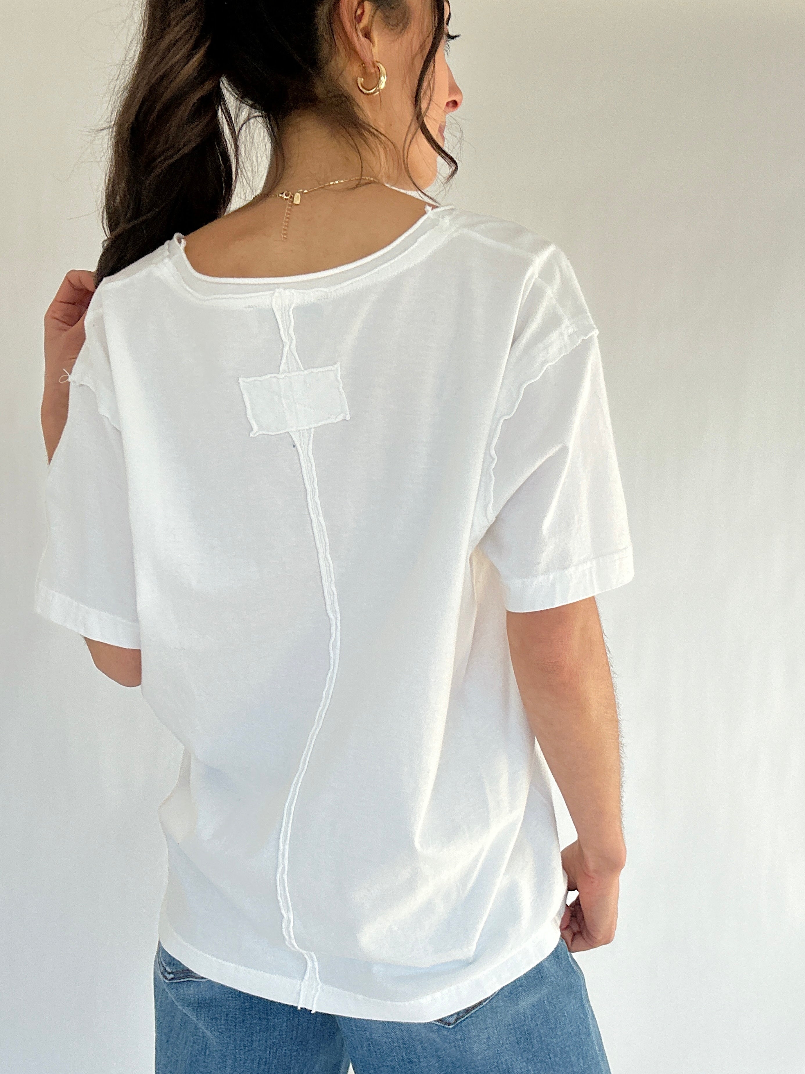 Person wearing a white tee with jeans from back with a plain background