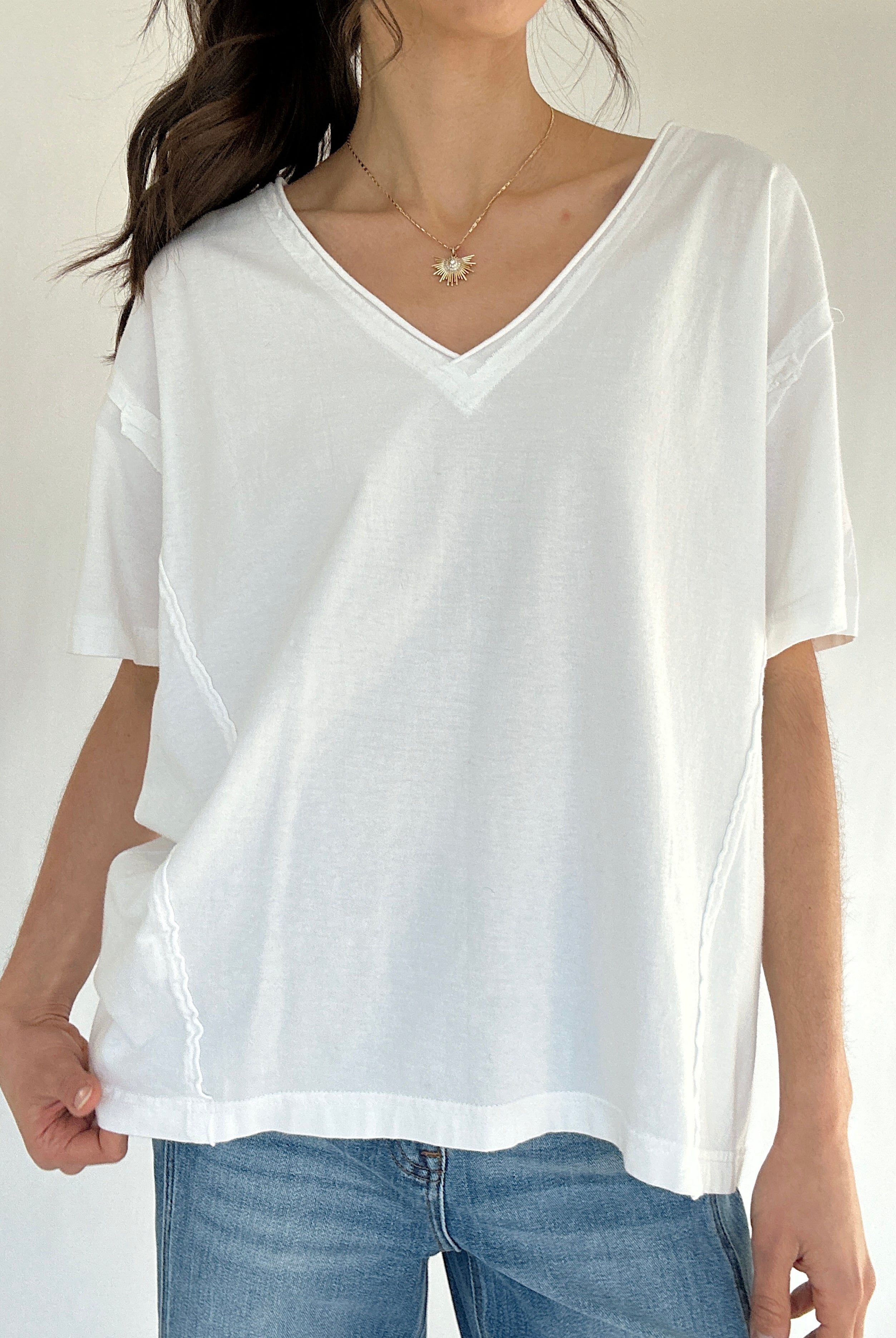 Person wearing a white oversized t-shirt and blue jeans on a plain background