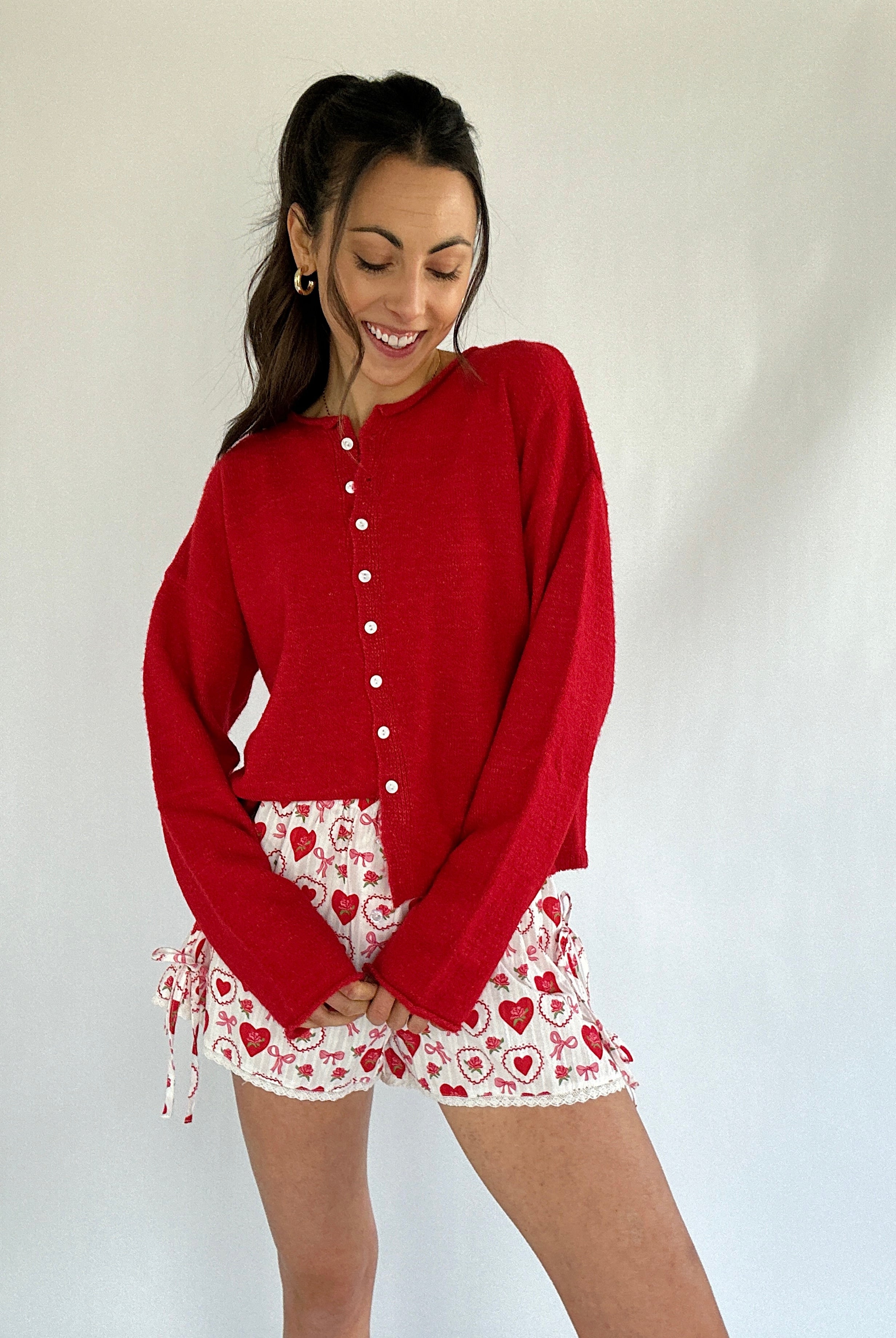 Woman wearing a red cardigan and patterned shorts against a white background