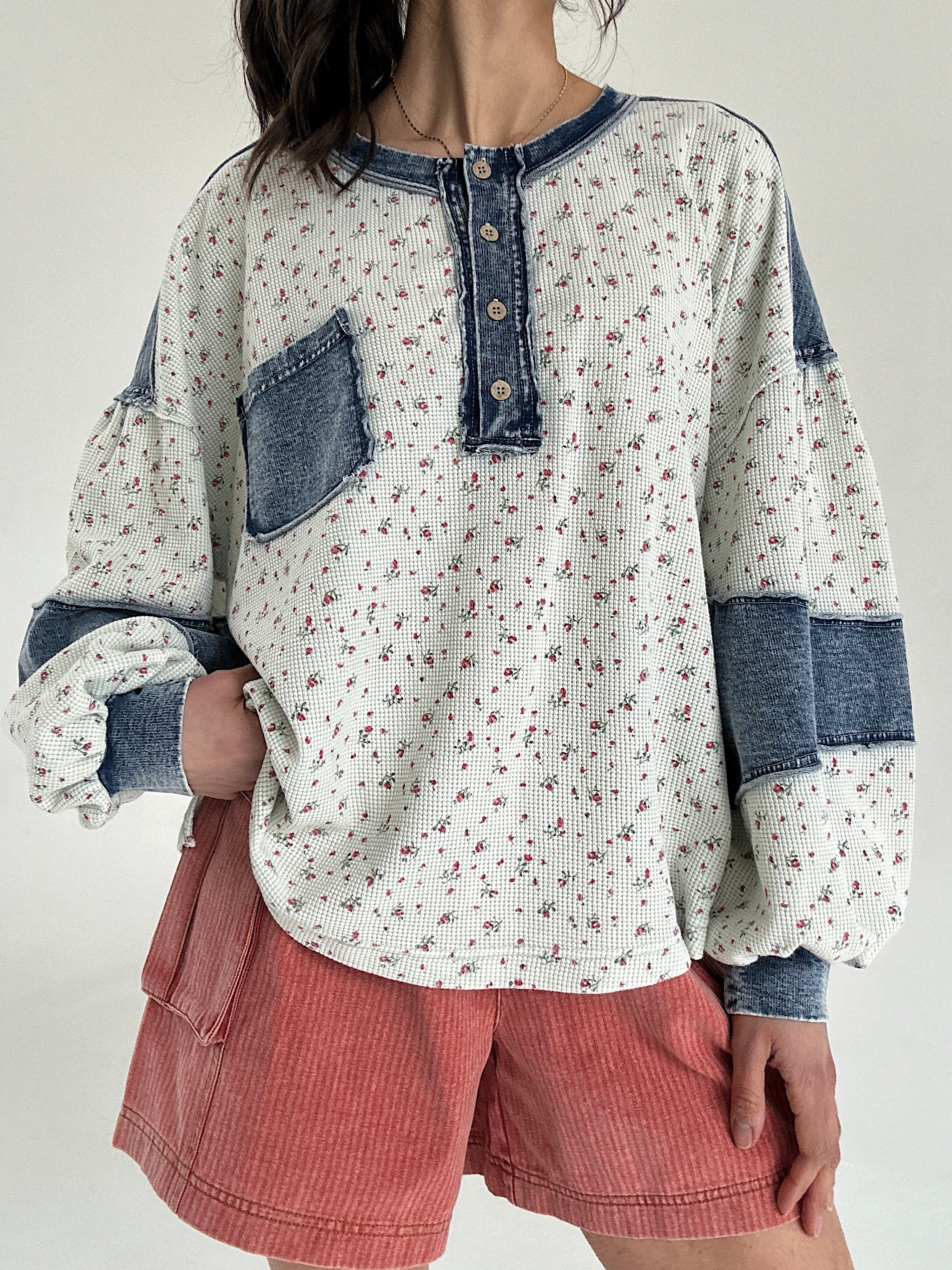 Person wearing a floral top with denim sleeve patches and rust shorts on a plain background