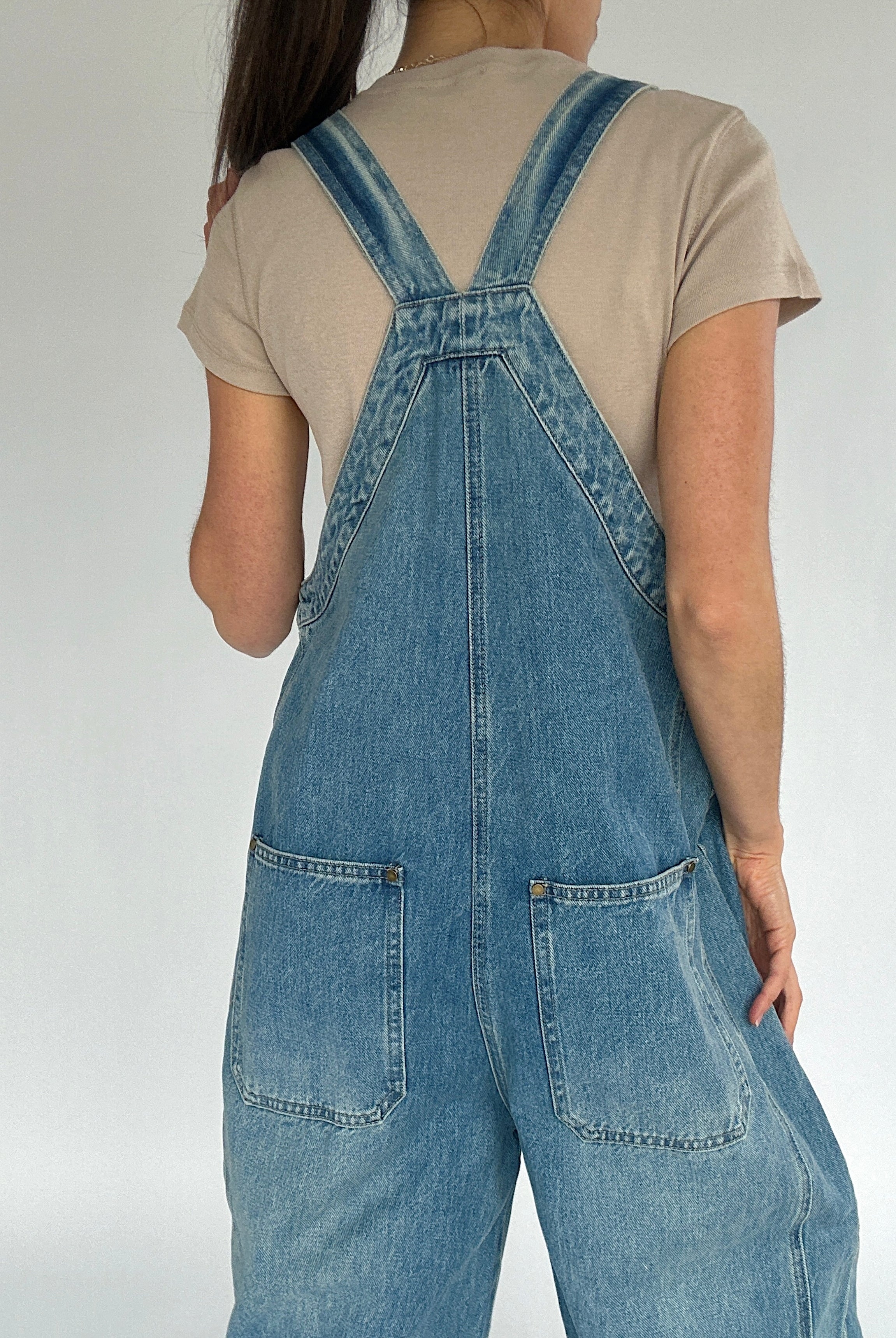 Person wearing blue denim overalls on a plain background back view