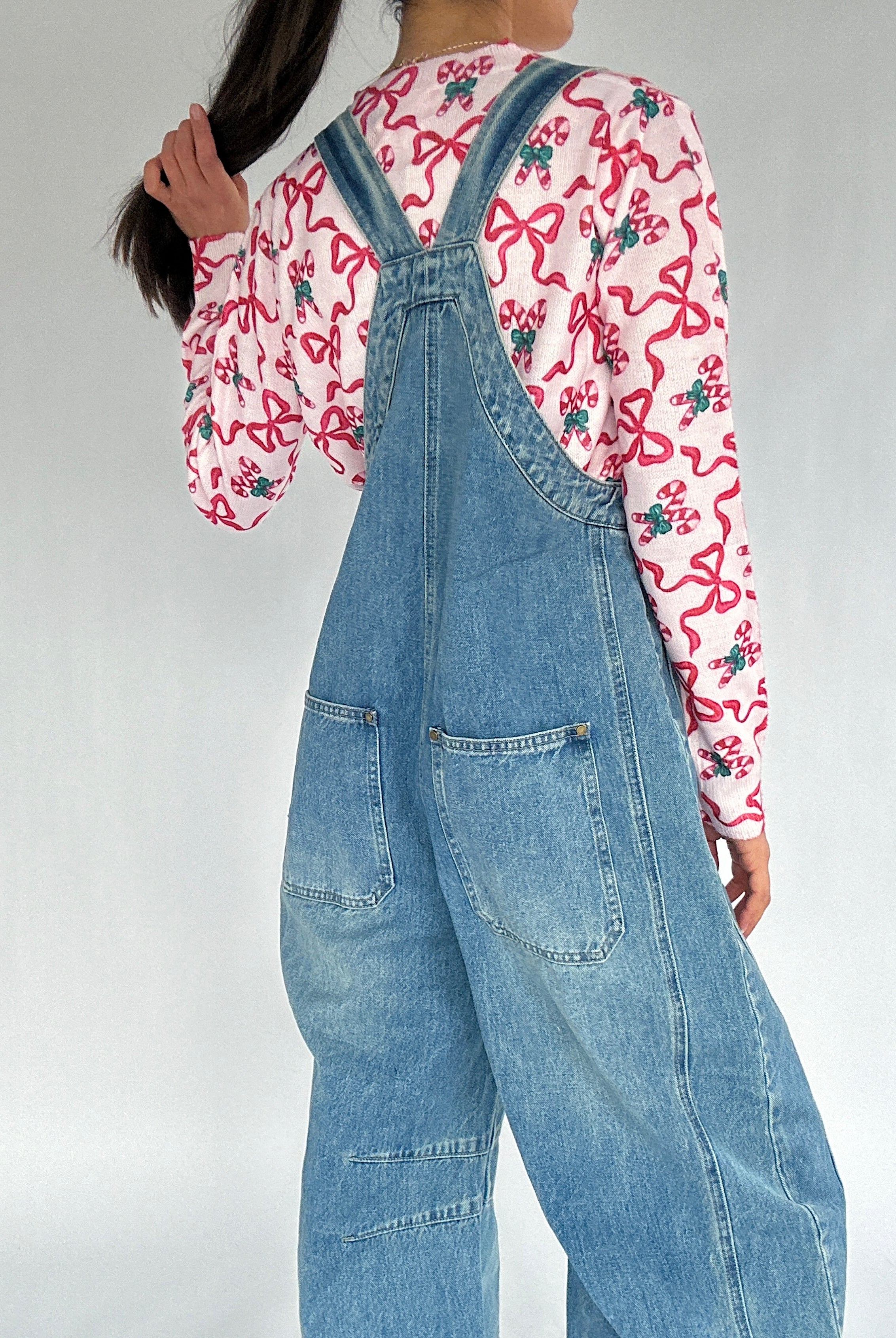 Person wearing a pink candy cane shirt and blue denim overalls on a plain background showing back