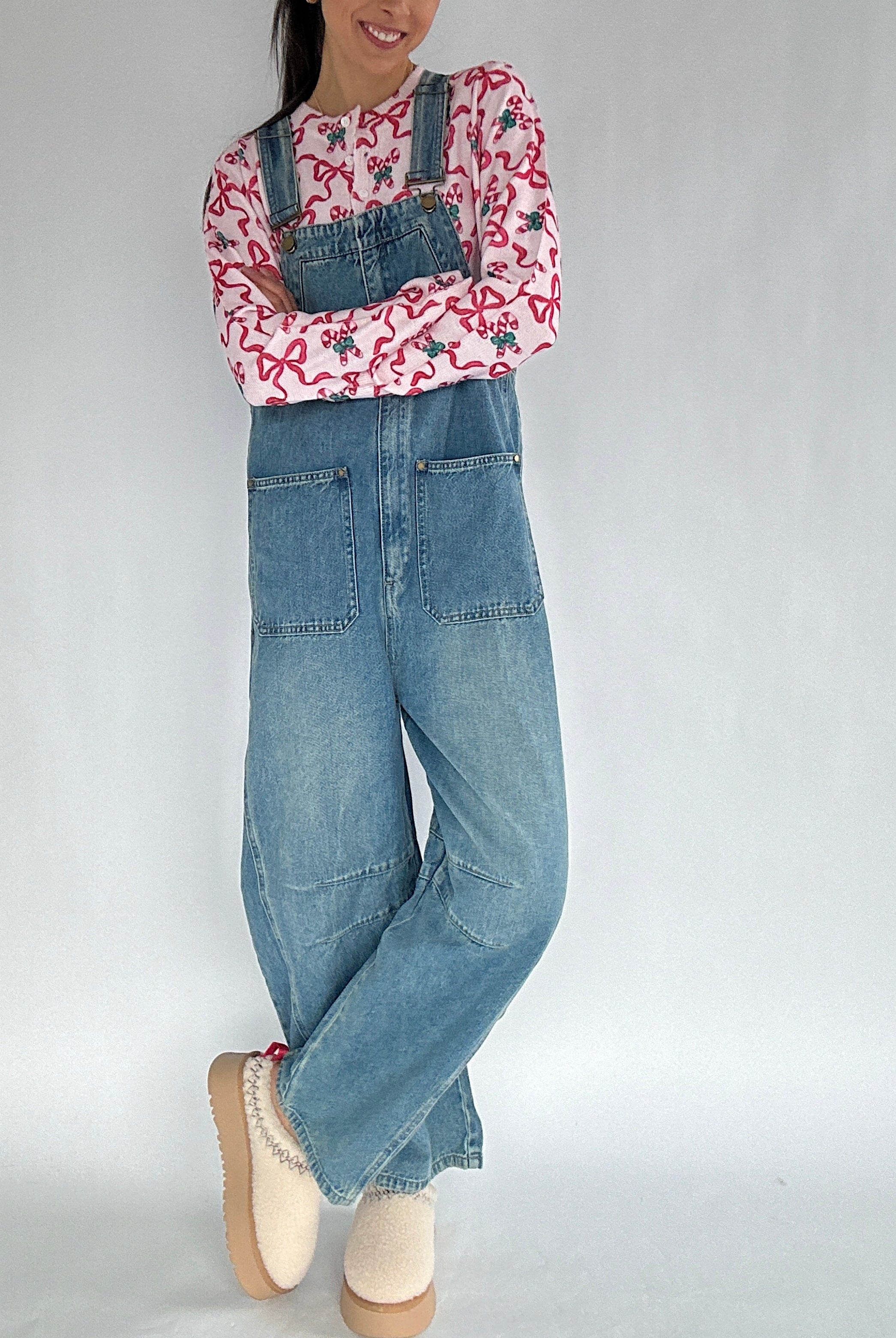 Person wearing a printed top and denim overalls on a plain background with arms crossed