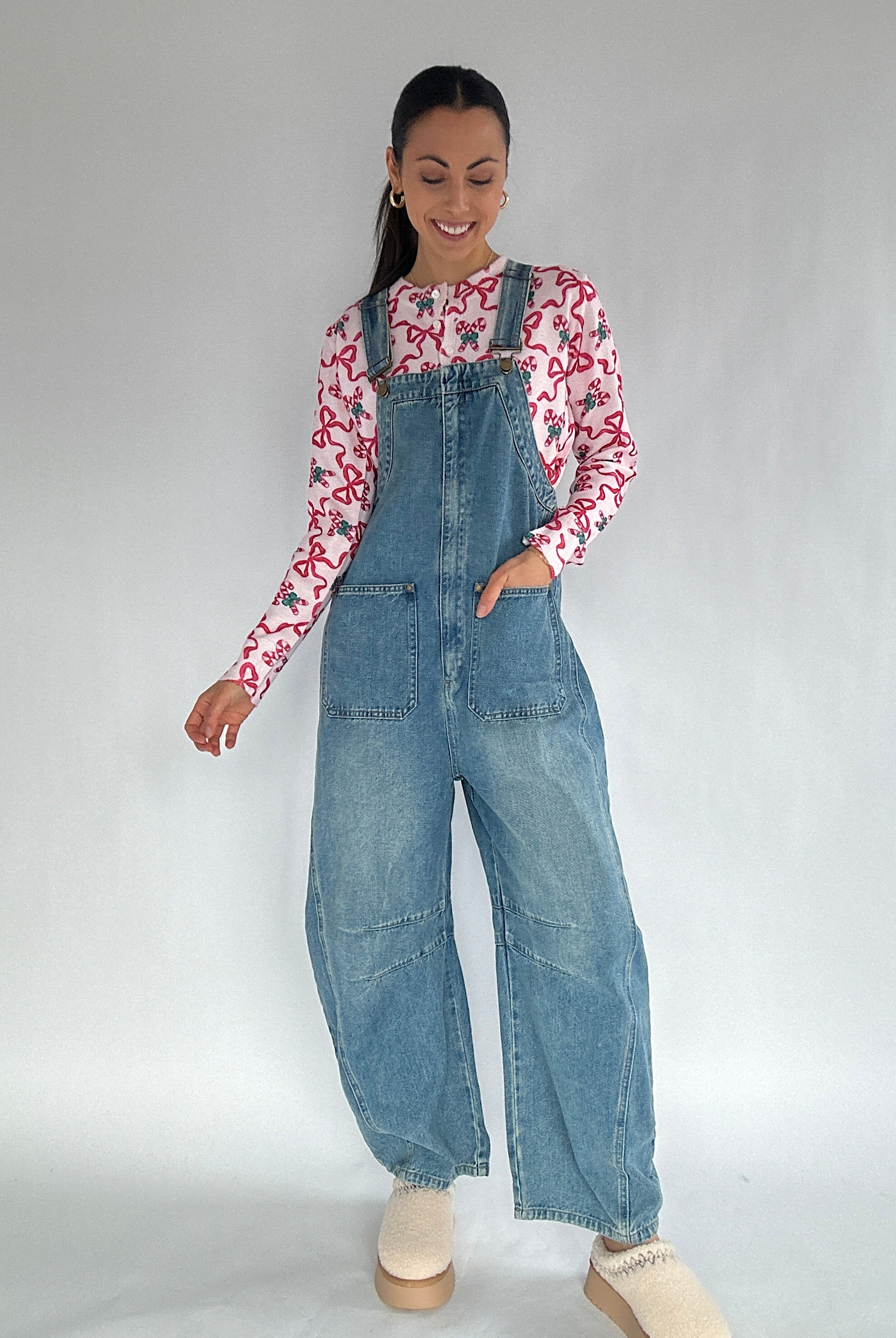 Woman wearing a denim overalls and a patterned shirt on a plain background