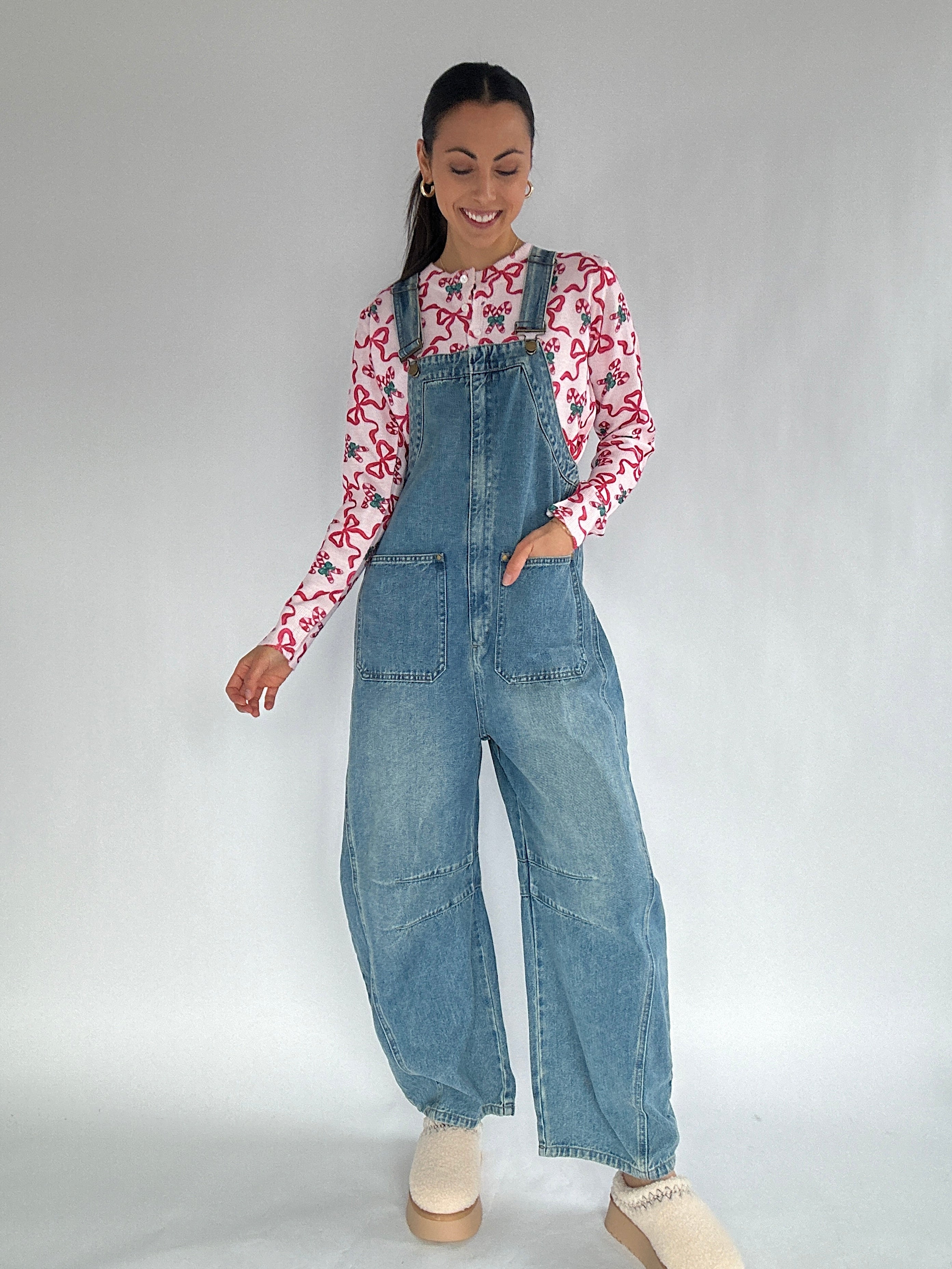 Woman wearing a denim overalls and a patterned shirt on a plain background