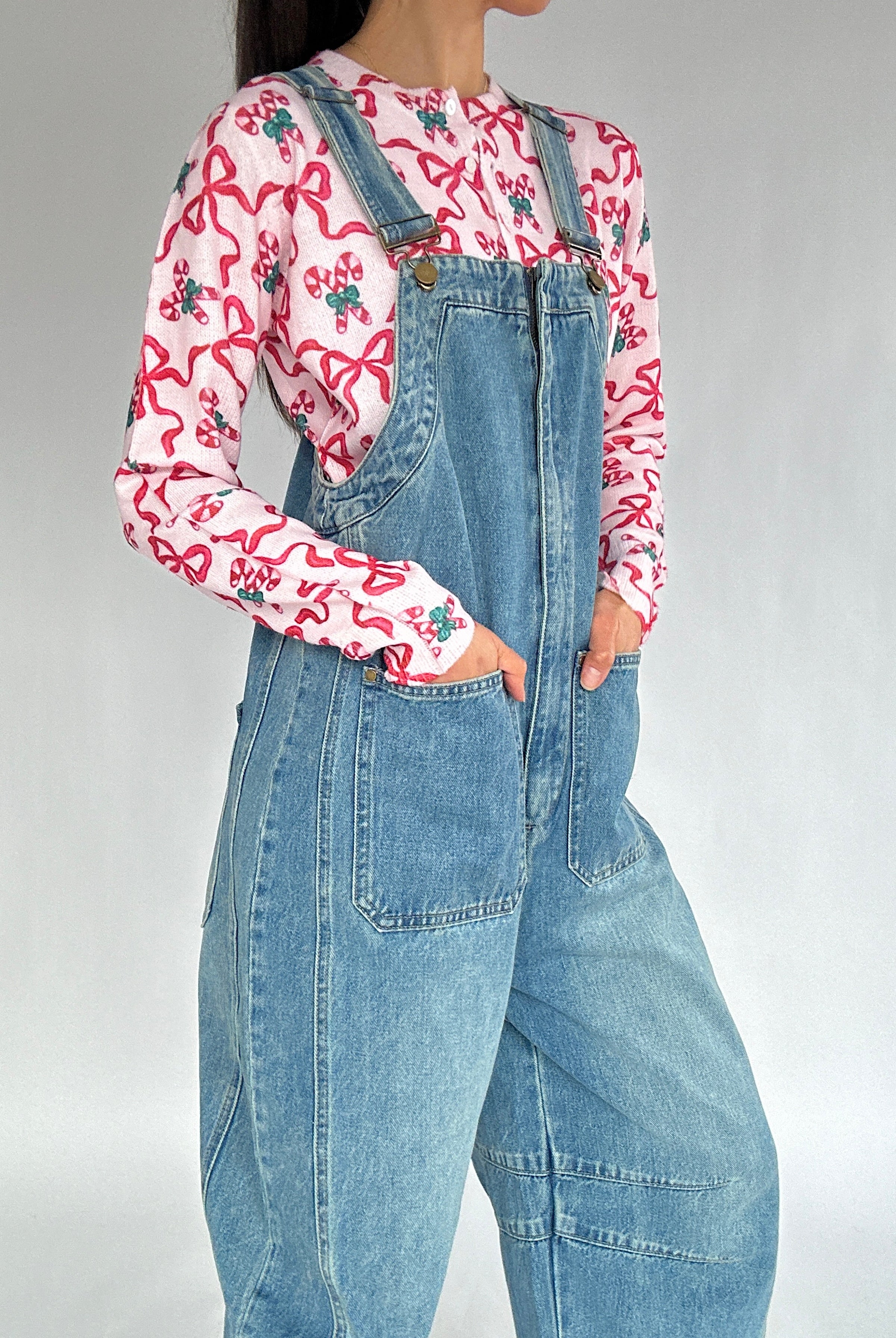 Person wearing a candy cane print cardigan and denim overalls on a plain background showing front patch pockets