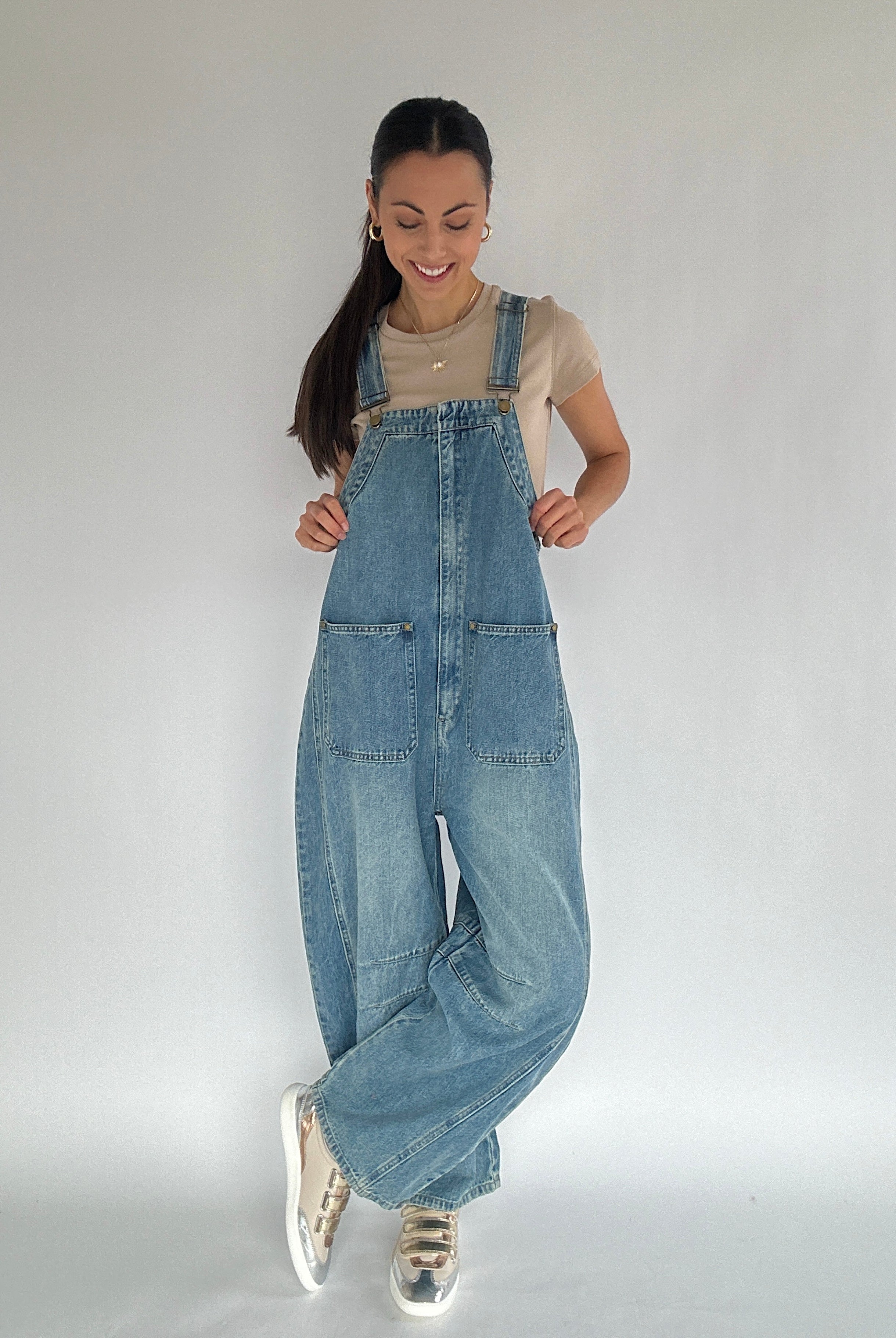 Person wearing blue barrel denim overalls on a plain background