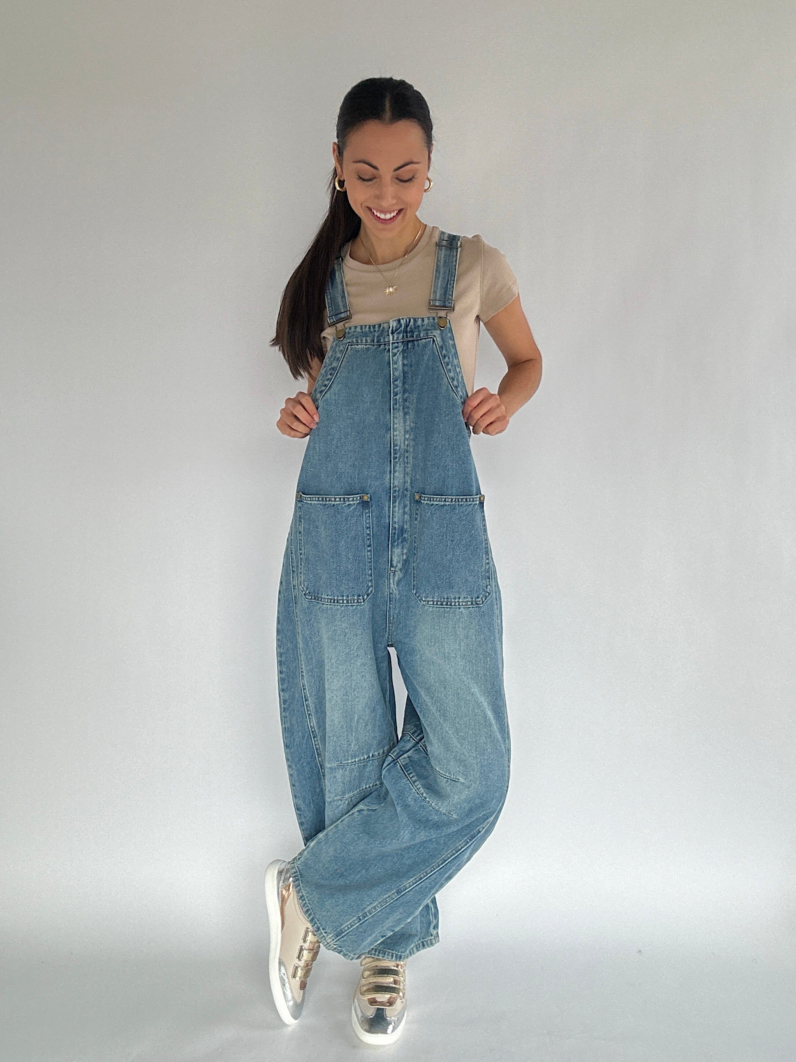 Person wearing blue barrel denim overalls on a plain background