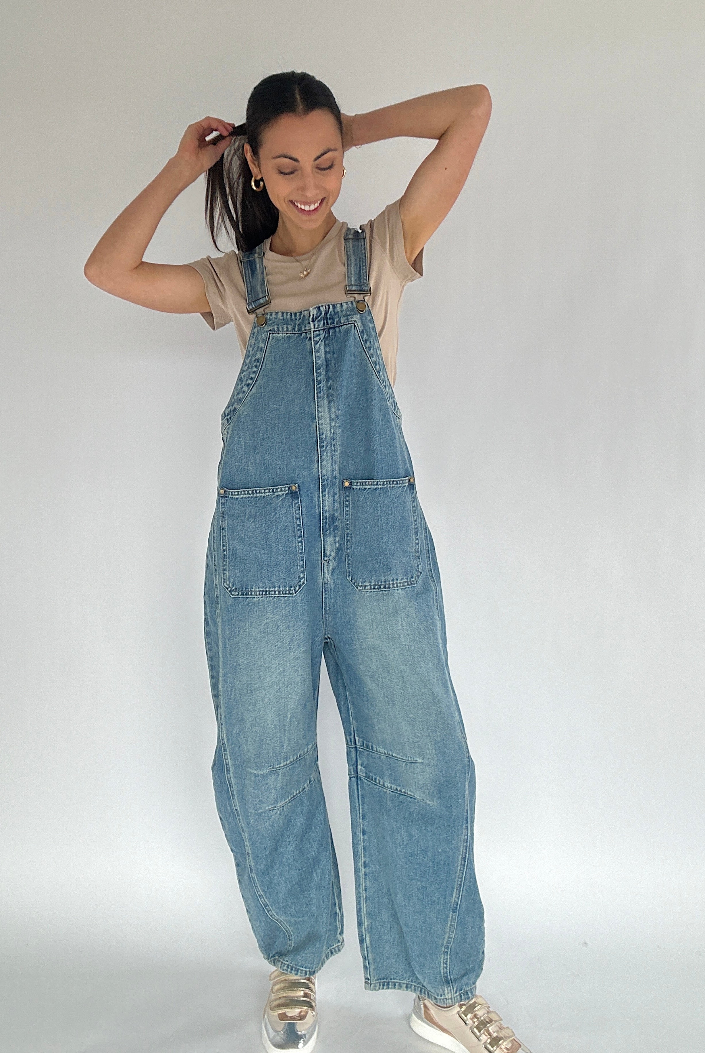 Person wearing blue denim overalls with a barrel silhouette on a plain background