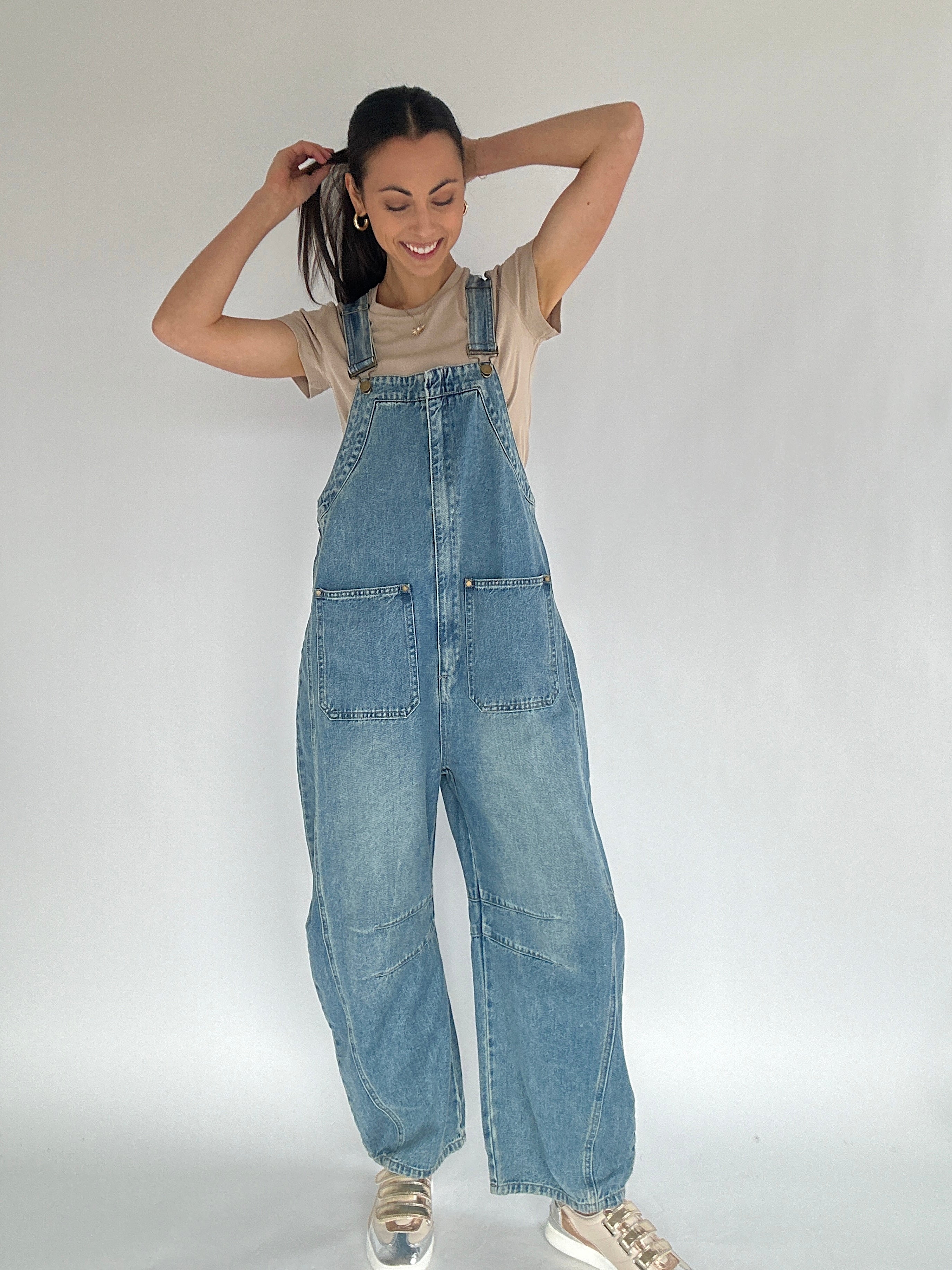 Person wearing blue denim overalls with a barrel silhouette on a plain background